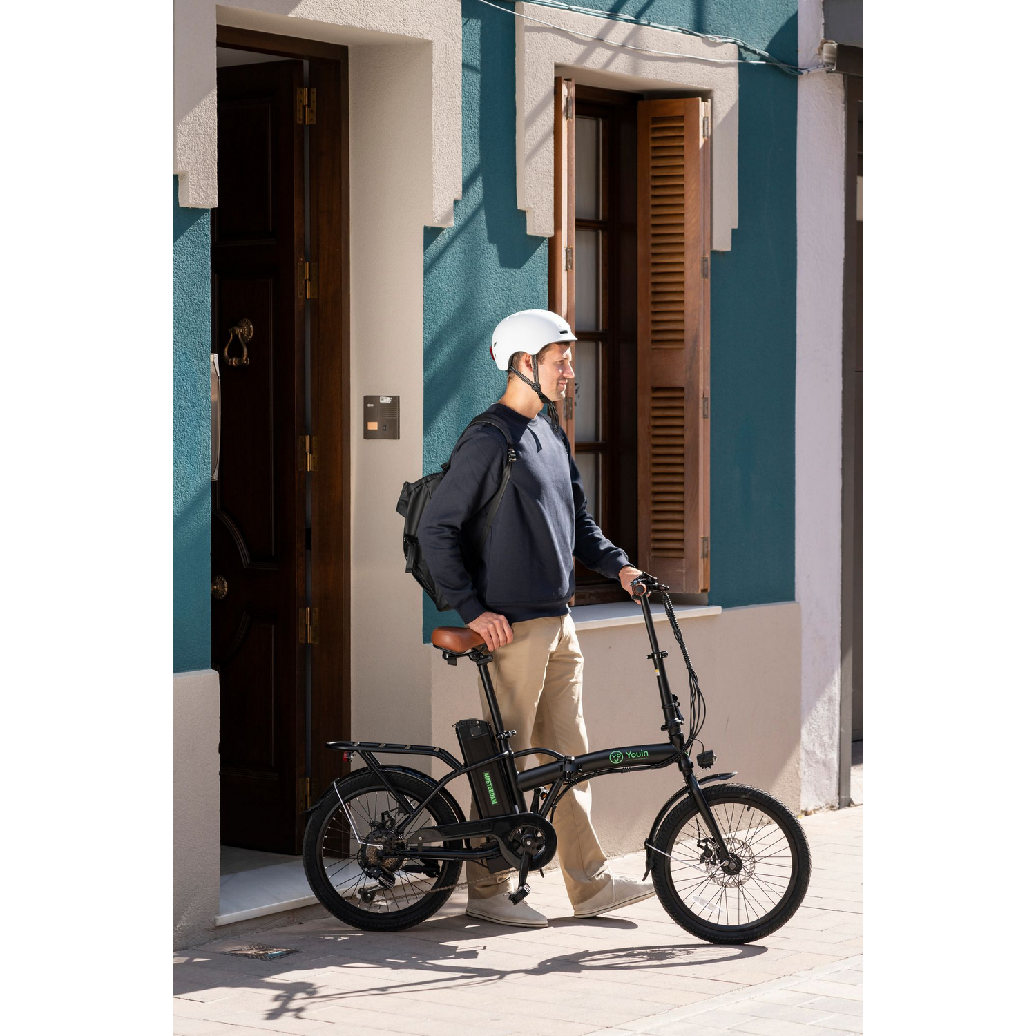 Hombre con casco en bicicleta negra, cerca de edificio azul y blanco.