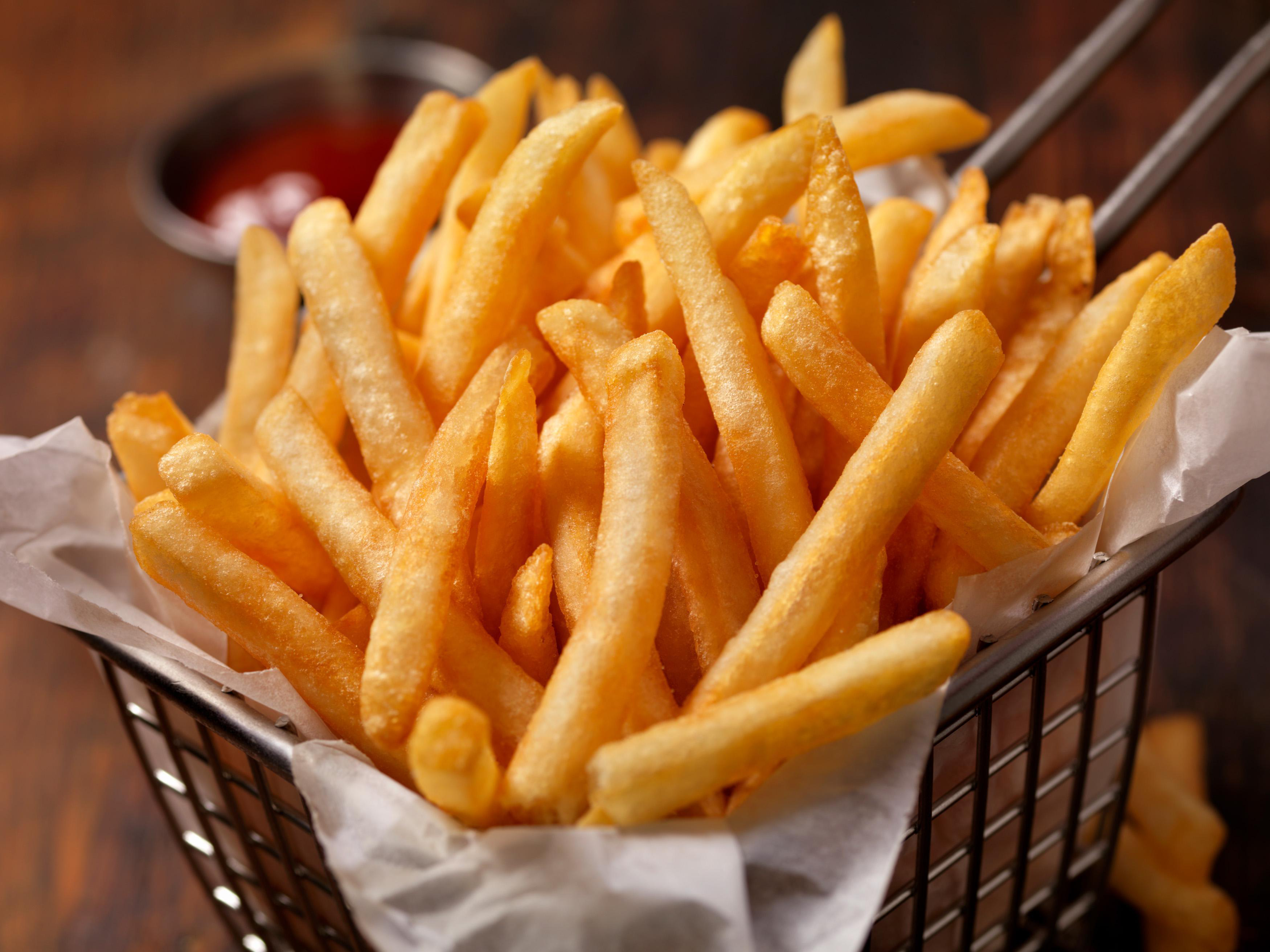 Ein Korb goldener Pommes Frites mit einer kleinen Schüssel Ketchup daneben.