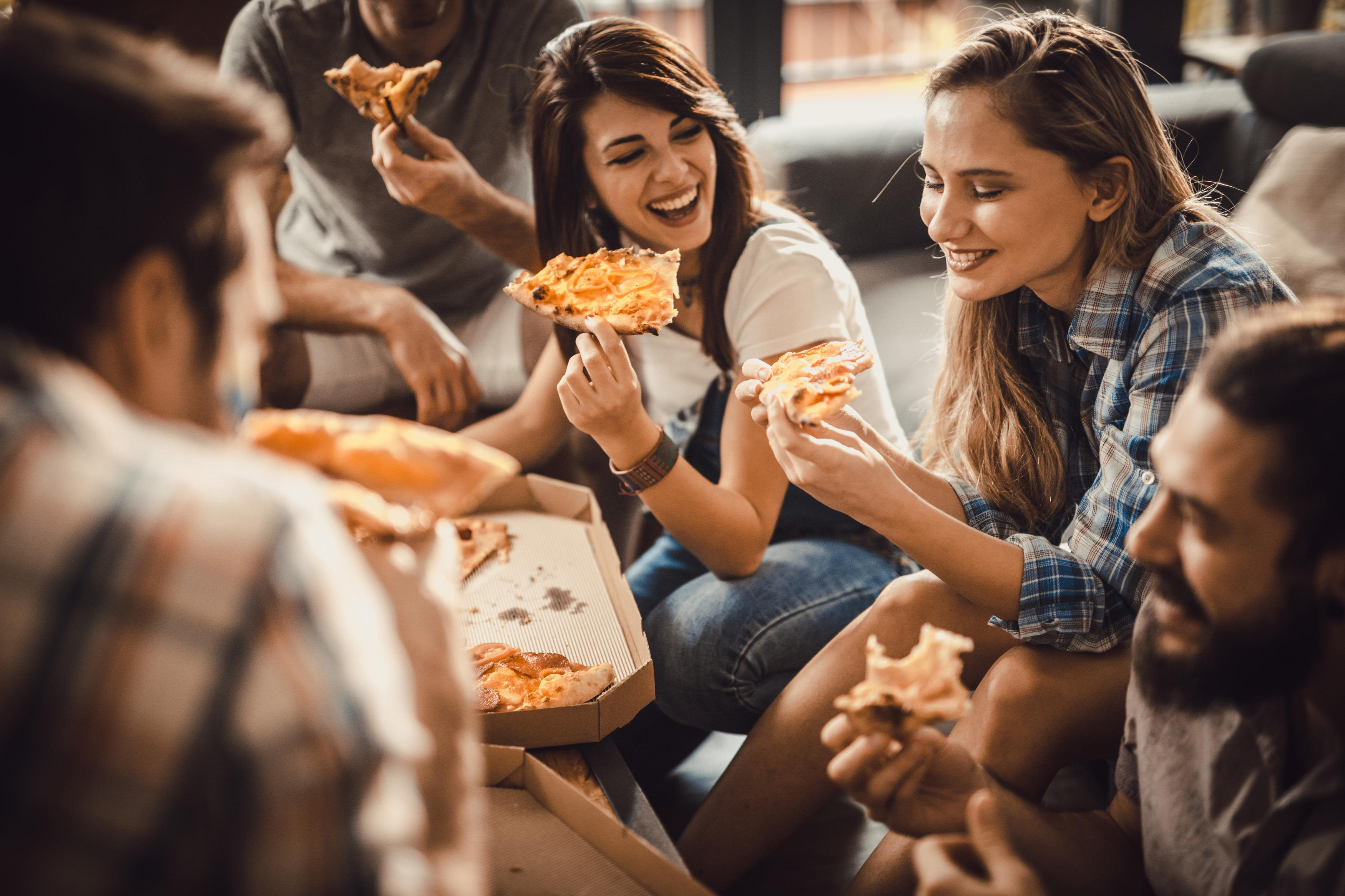 Eine Gruppe von Leuten, die lachen, während sie Pizza aus einer Schachtel essen.