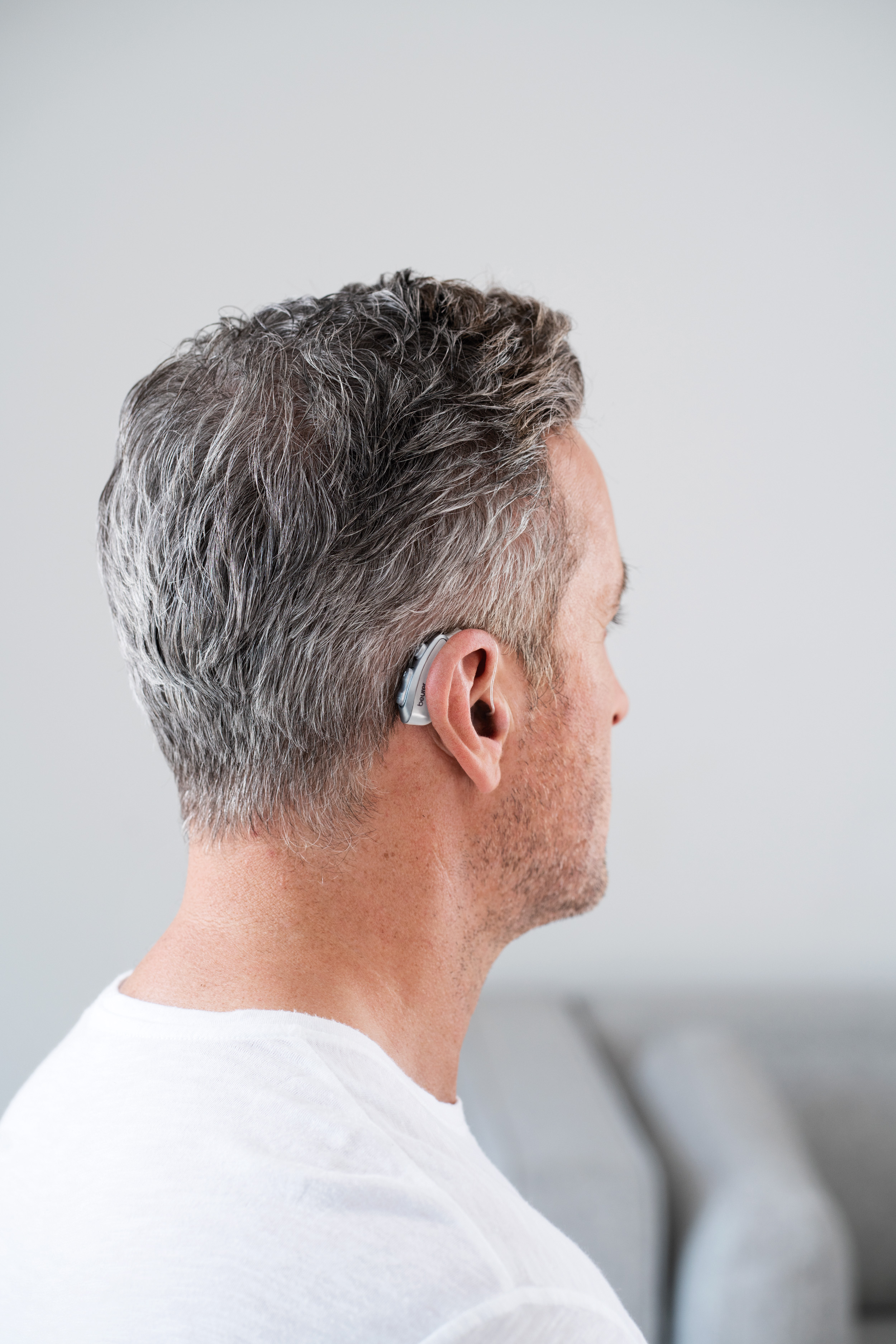 Mann mit grauem Haar, von der Seite betrachtet, trägt ein Hörgerät.