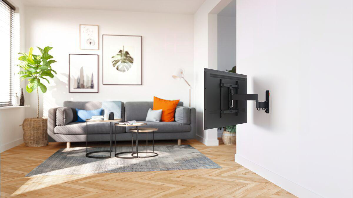 Wohnzimmer mit grauem Sofa, gerahmten Bildern und einem großen Fernseher an einer weißen Wand.