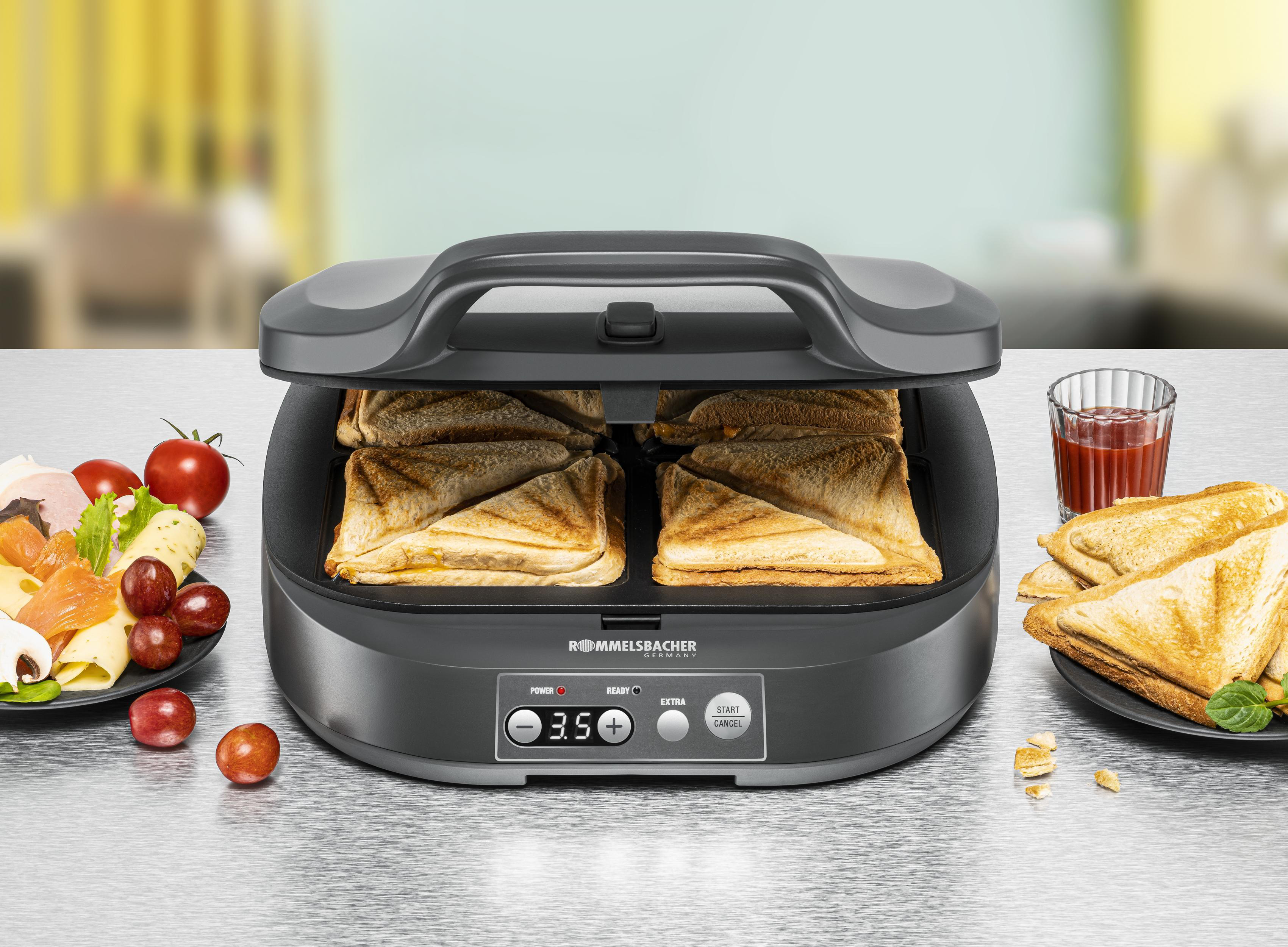 Toaster mit Sandwiches, Obst und Tomatensaft auf glänzender Oberfläche. Der Toaster ist offen.