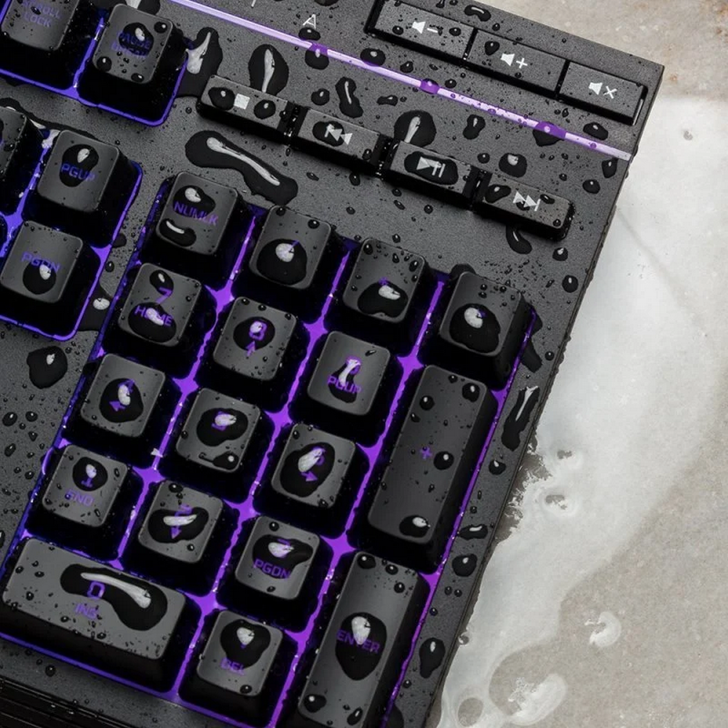 Primer plano de un teclado negro con retroiluminación morada y gotas de agua en las teclas.