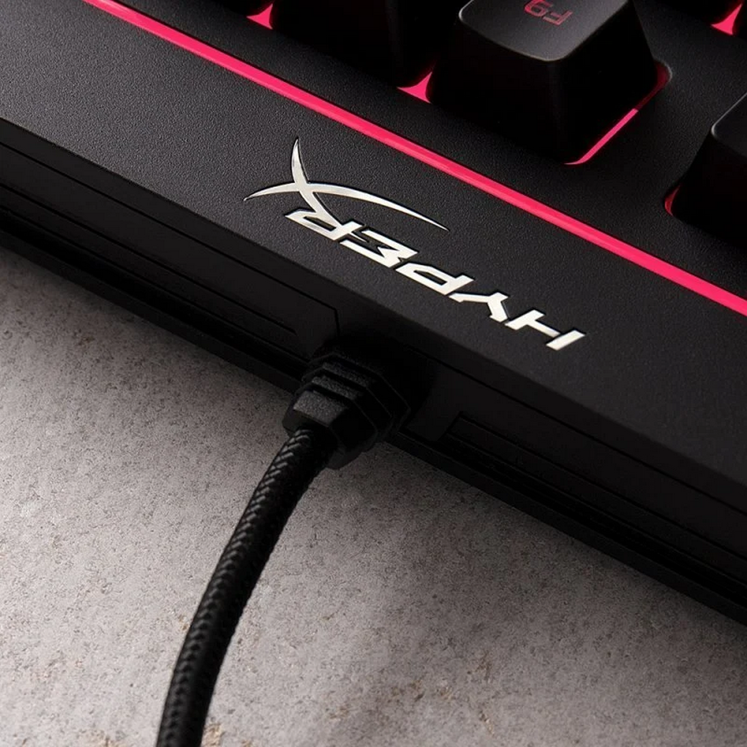Teclado HyperX negro con iluminación rosa. Fondo: oscuro.