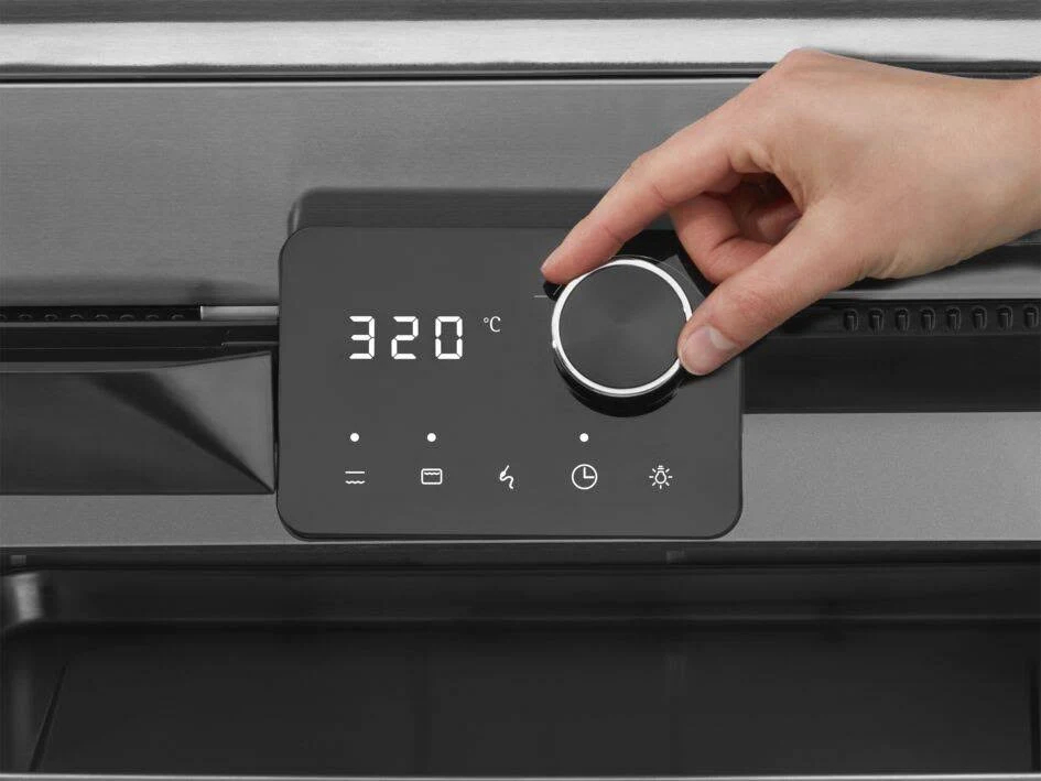 Eine Hand dreht einen schwarzen Drehregler an einem Backofen-Bedienfeld; 320°C werden angezeigt.