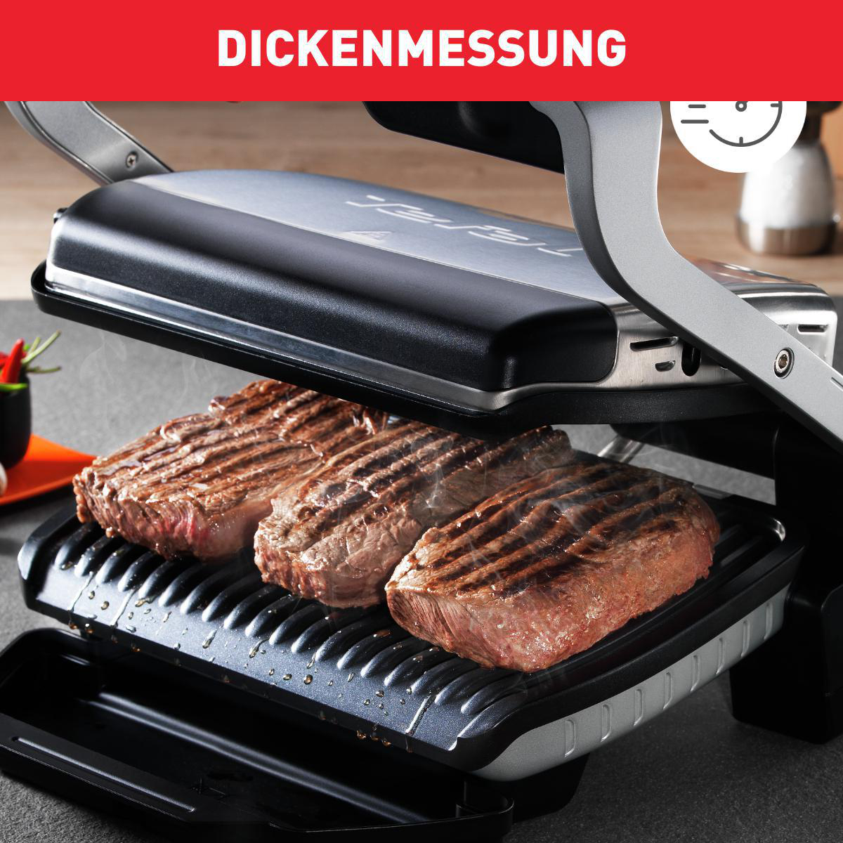 Ein Grill mit drei gegrillten Steaks. Der Grill ist geöffnet, mit rotem Banner oben.