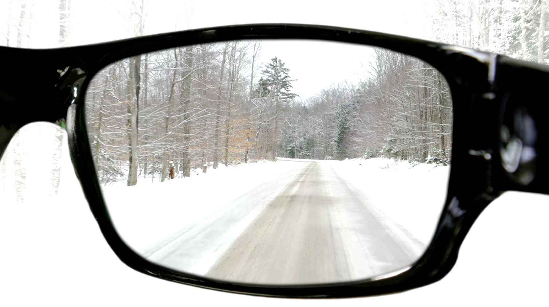 Blick durch eine Brille auf eine schneebedeckte Straße durch einen Wald. Bäume säumen die Straße. Schnee bedeckt den Boden.