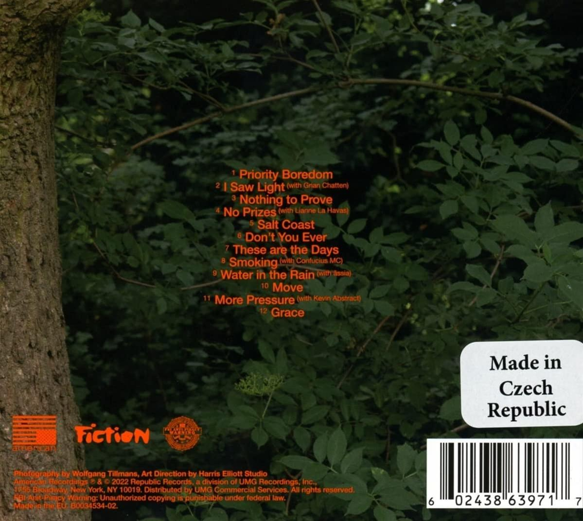 Albumcover im Wald. Text mit Songtiteln. Grünes Laub und ein Baumstamm sind sichtbar.
