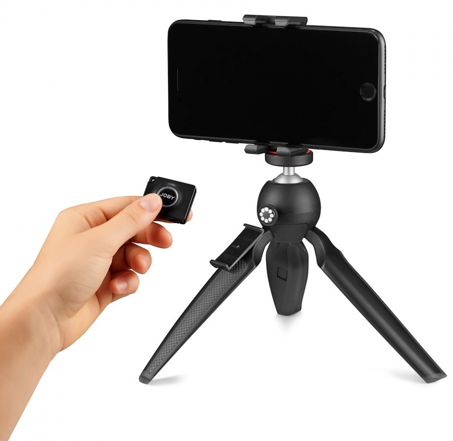 Hand met afstandsbediening naast een smartphone op een statief. Statief is zwart.