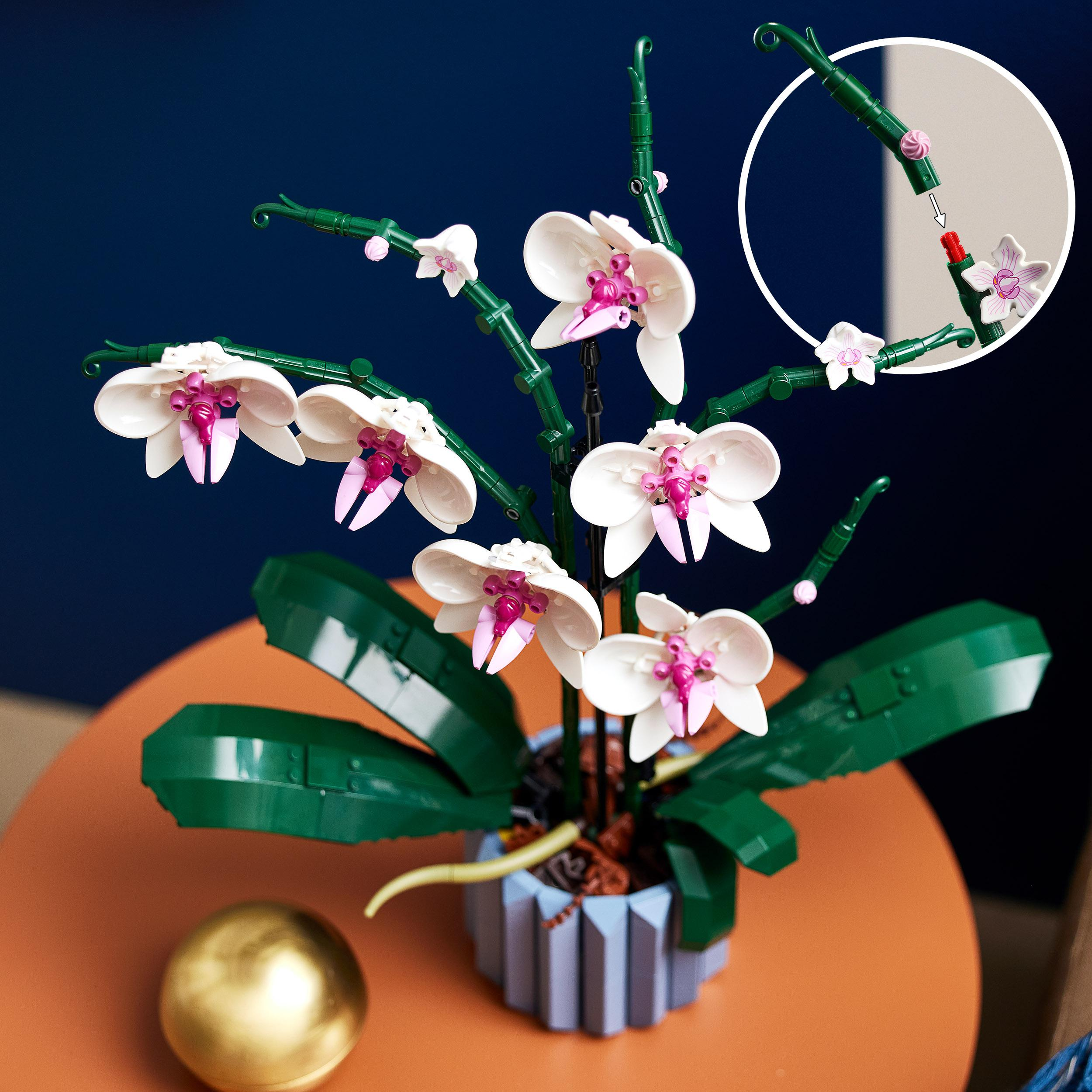 Eine LEGO-Orchideenpflanze mit weißen und rosa Blüten in einer blauen Vase auf einem Tisch.