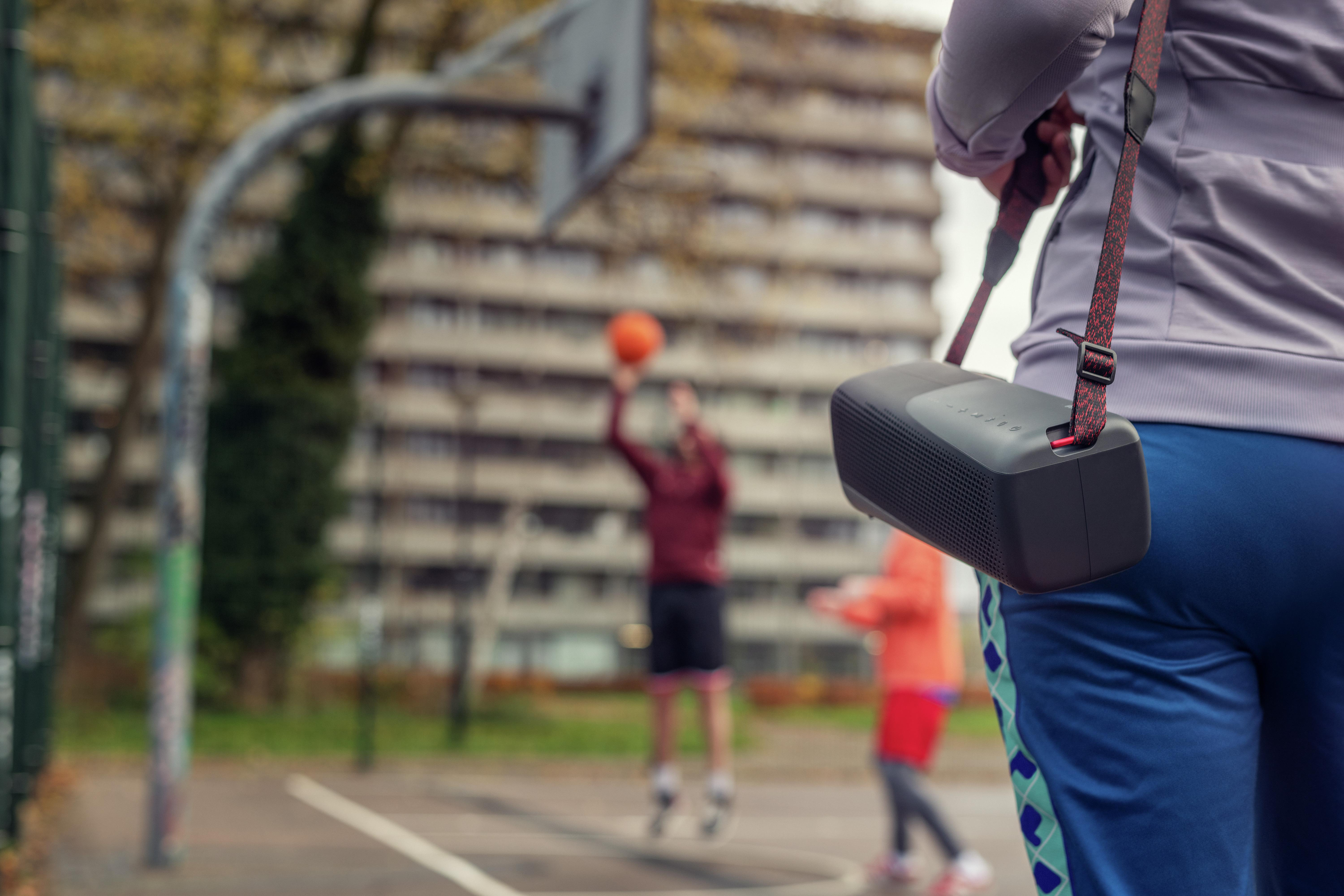 Person mit Lautsprecher, der an einem Gurt hängt, in der Nähe eines Basketballplatzes. Verschwommener Hintergrund.