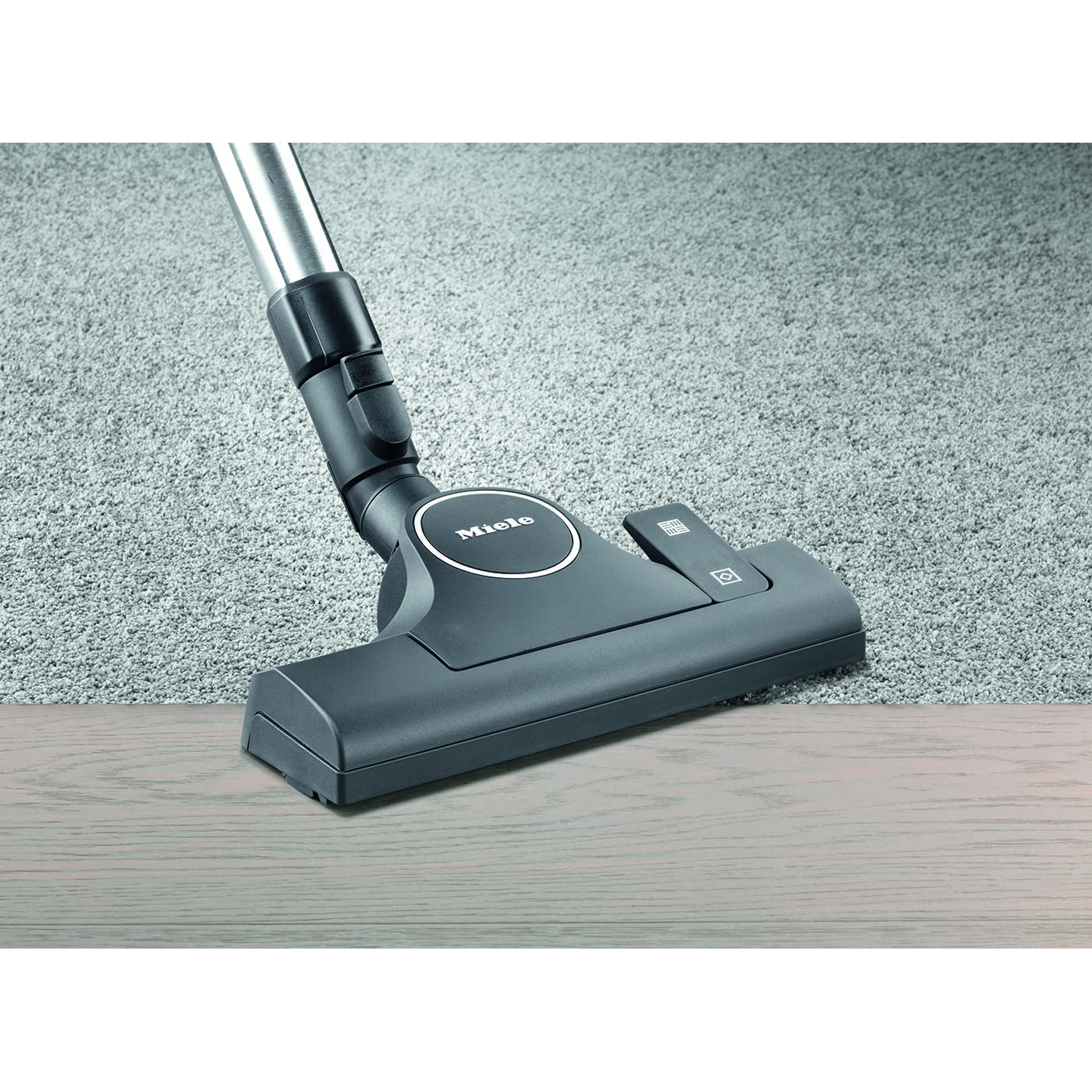 Primer plano de un cabezal de aspiradora sobre una alfombra gris claro, con un suelo de madera en primer plano.