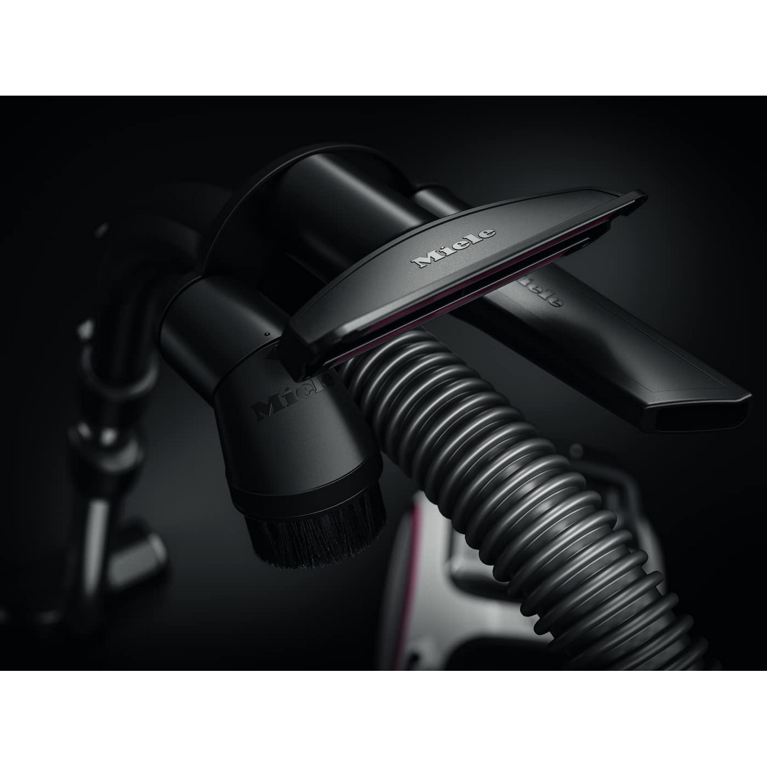 Primer plano de accesorios y manguera de aspiradora. Fondo negro. Marca Miele.