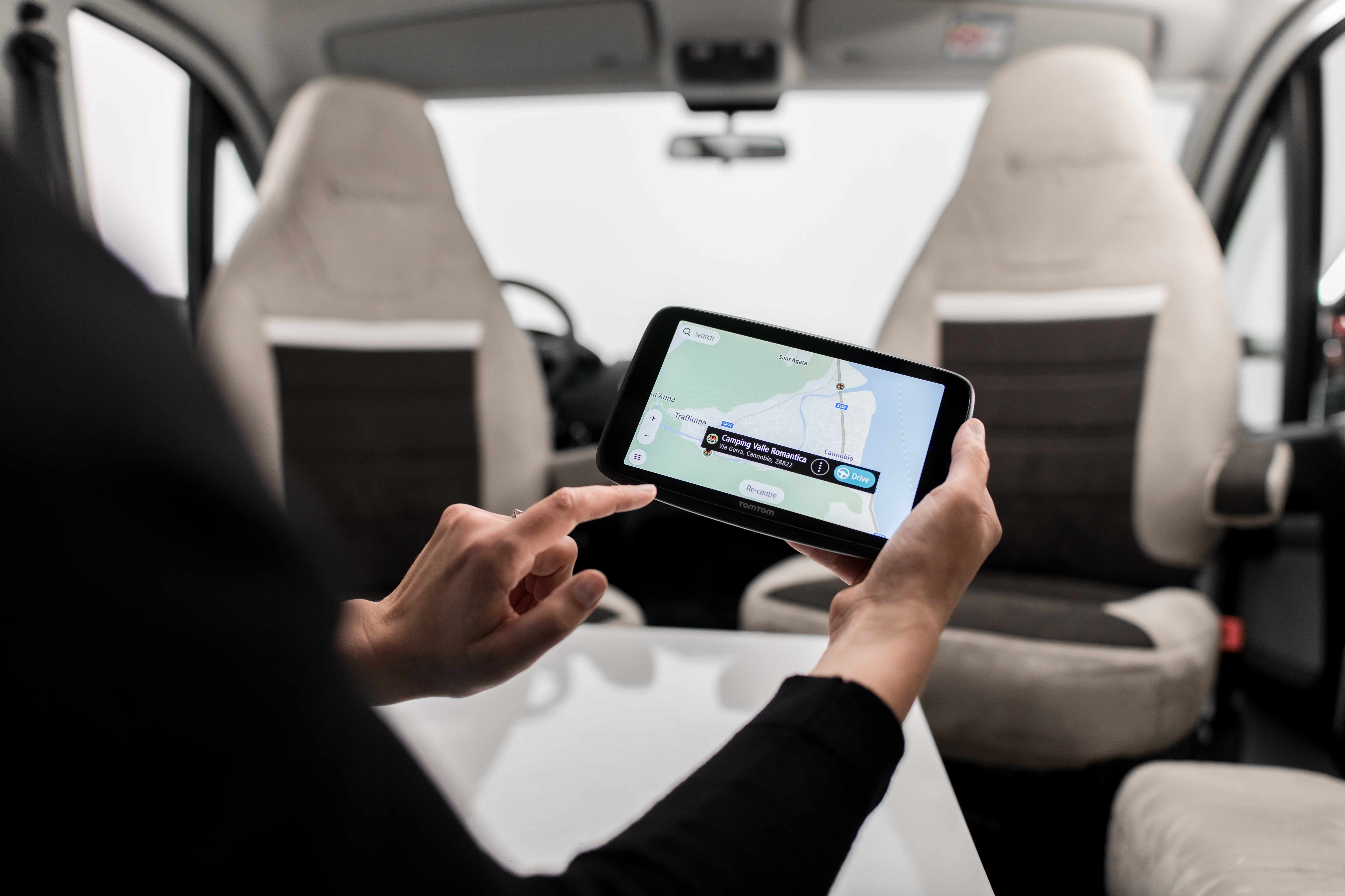 Person in einem Wohnmobil hält ein Telefon und navigiert mit einer Karten-App. Beiges Interieur.