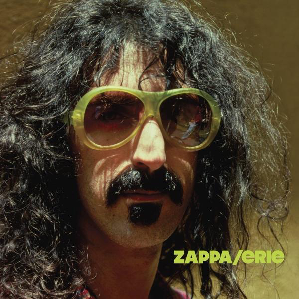 Frank Zappa mit gelben Sonnenbrillen, langen Haaren und Schnurrbart. Zappa/Erie-Text.
