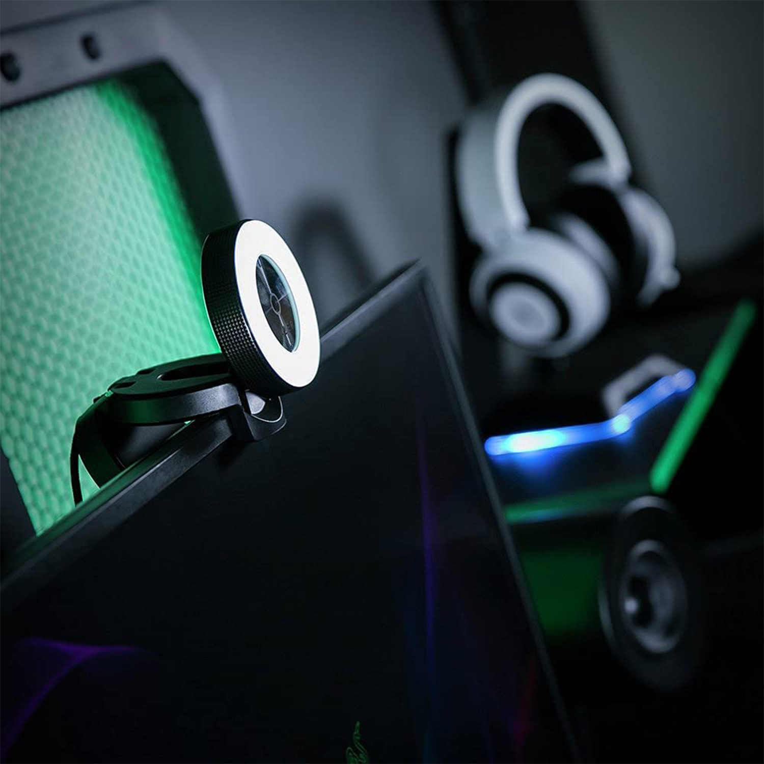 Una webcam con una luce ad anello su un monitor. Un auricolare è sullo sfondo.