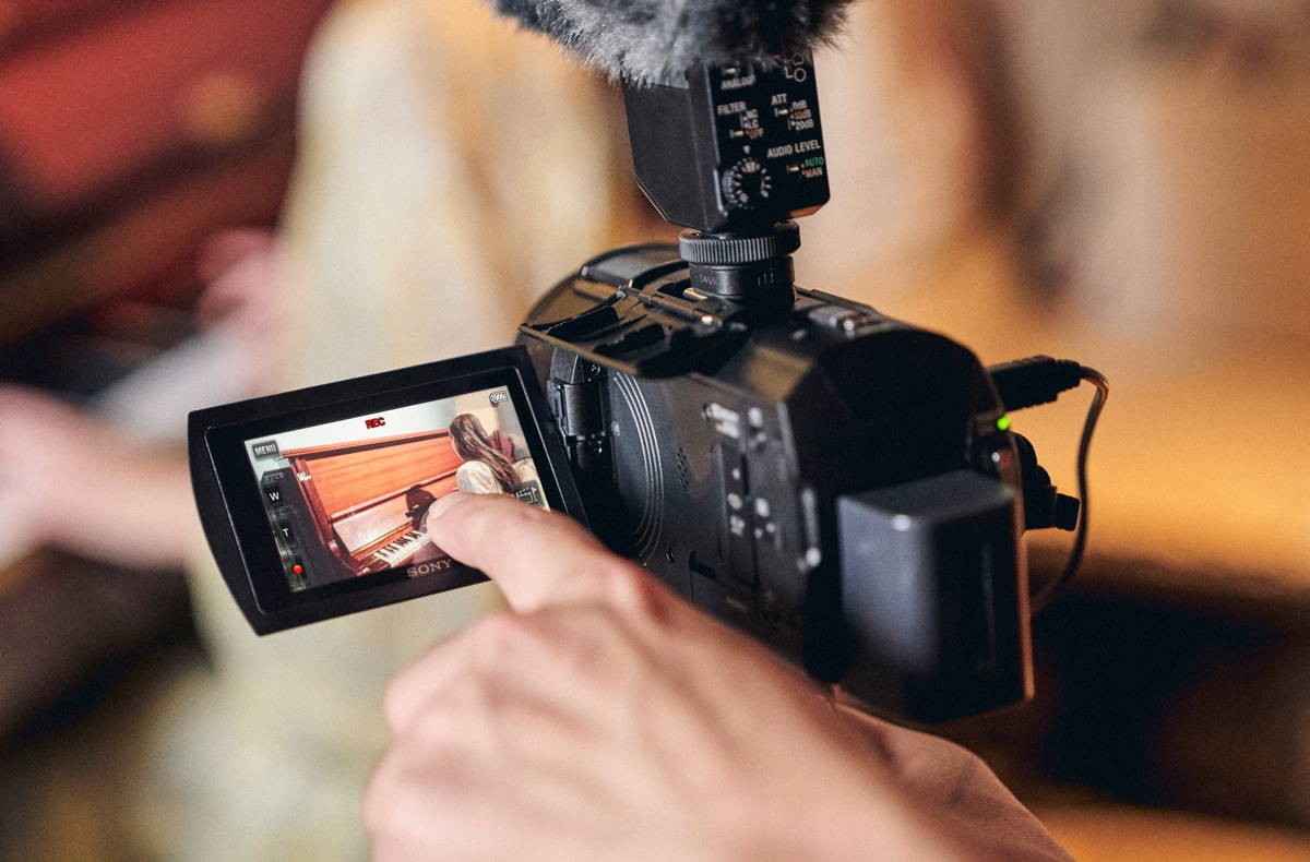 Persona filmando a un pianista con una videocámara. La pantalla muestra la grabación.