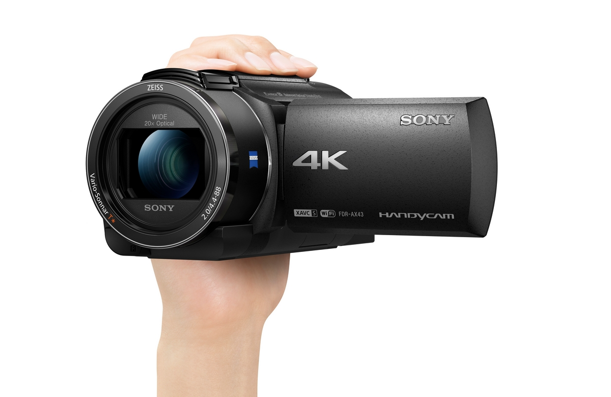 Mano sosteniendo una videocámara Sony 4K negra. La lente dice Zeiss, zoom óptico 20x y 4K.