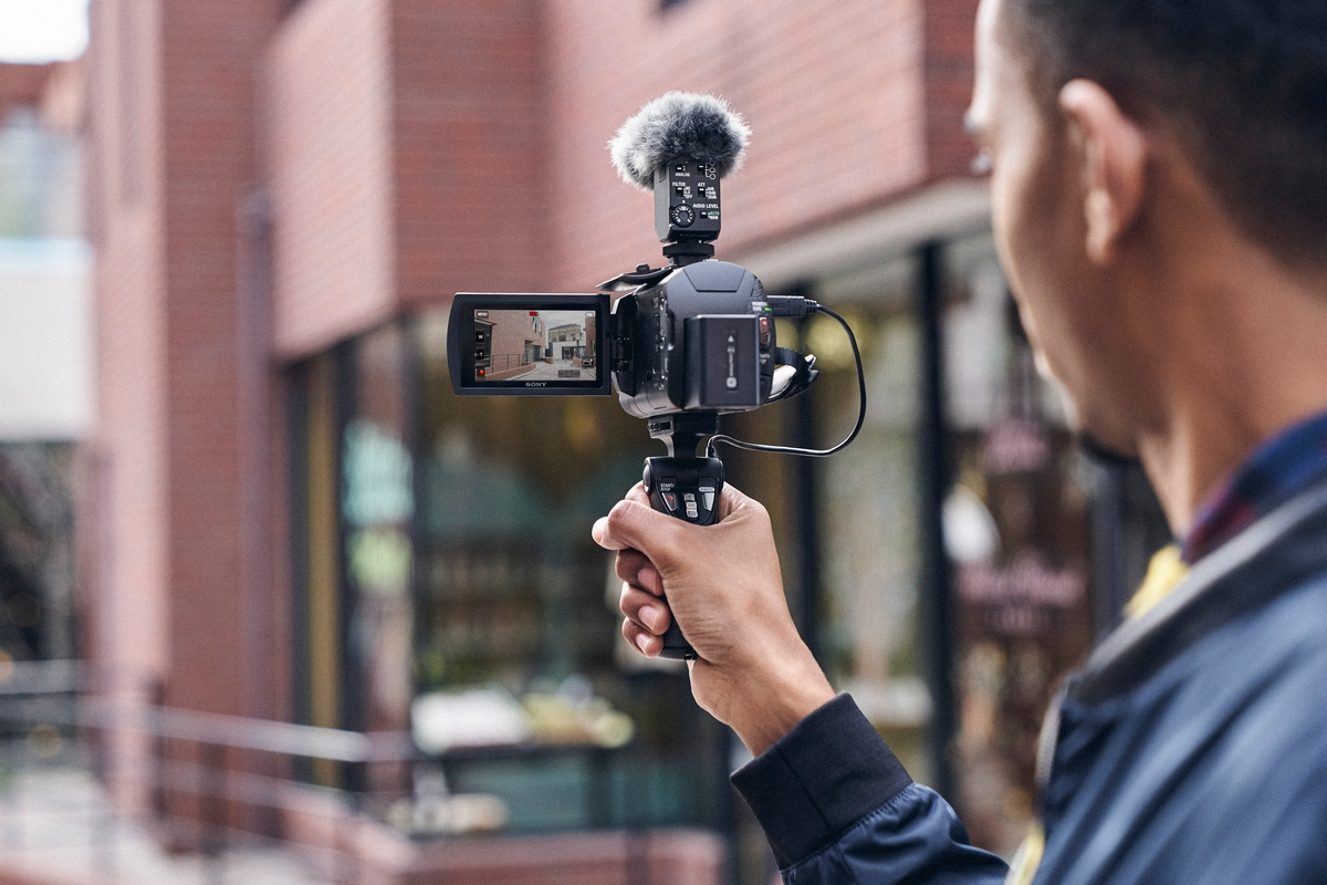 Persona sosteniendo una cámara de video con micrófono, grabando en una calle de la ciudad.