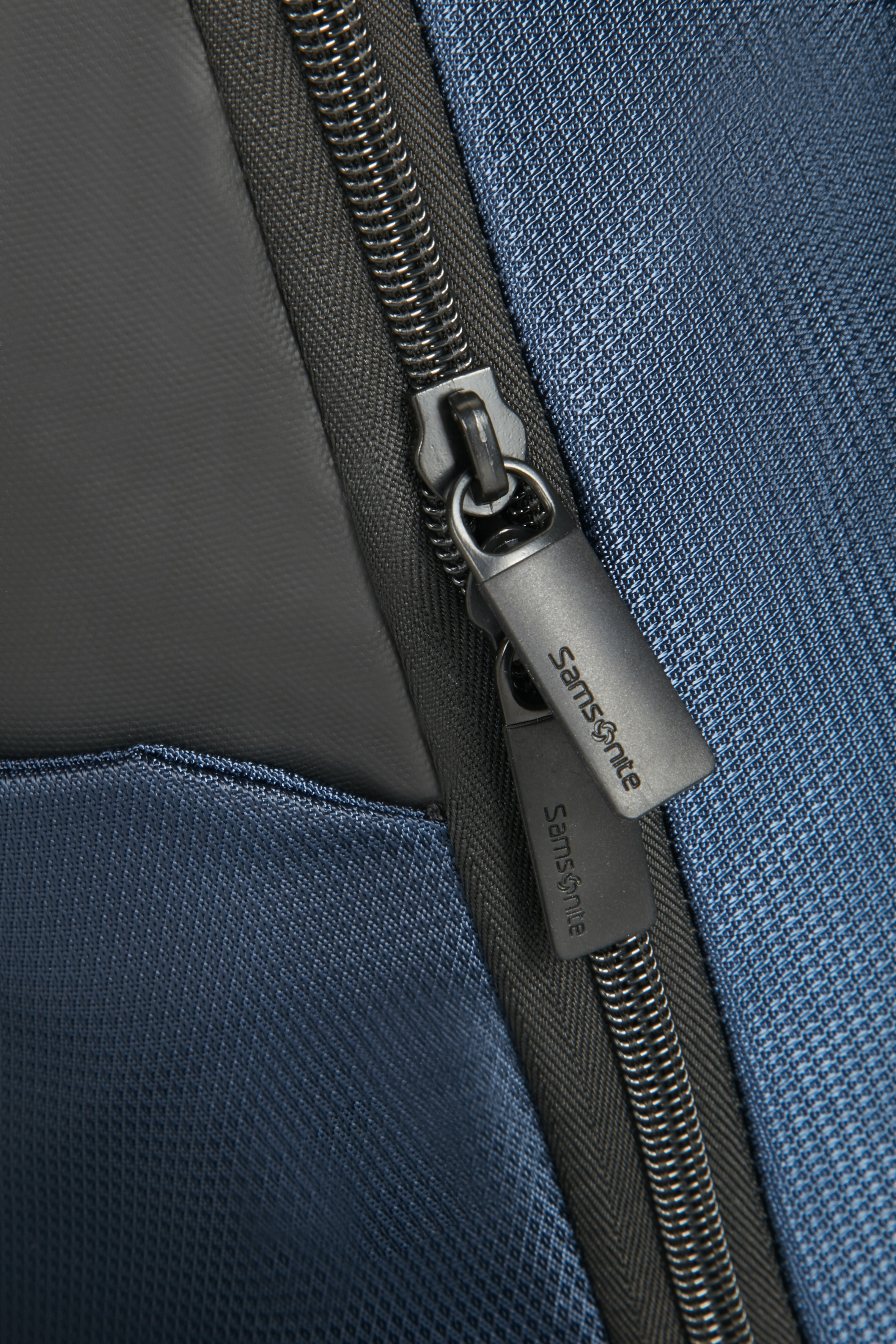 Samsonite sırt çantasının fermuarının yakından görünümü. Gümüş fermuar, koyu mavi ve gri malzeme.