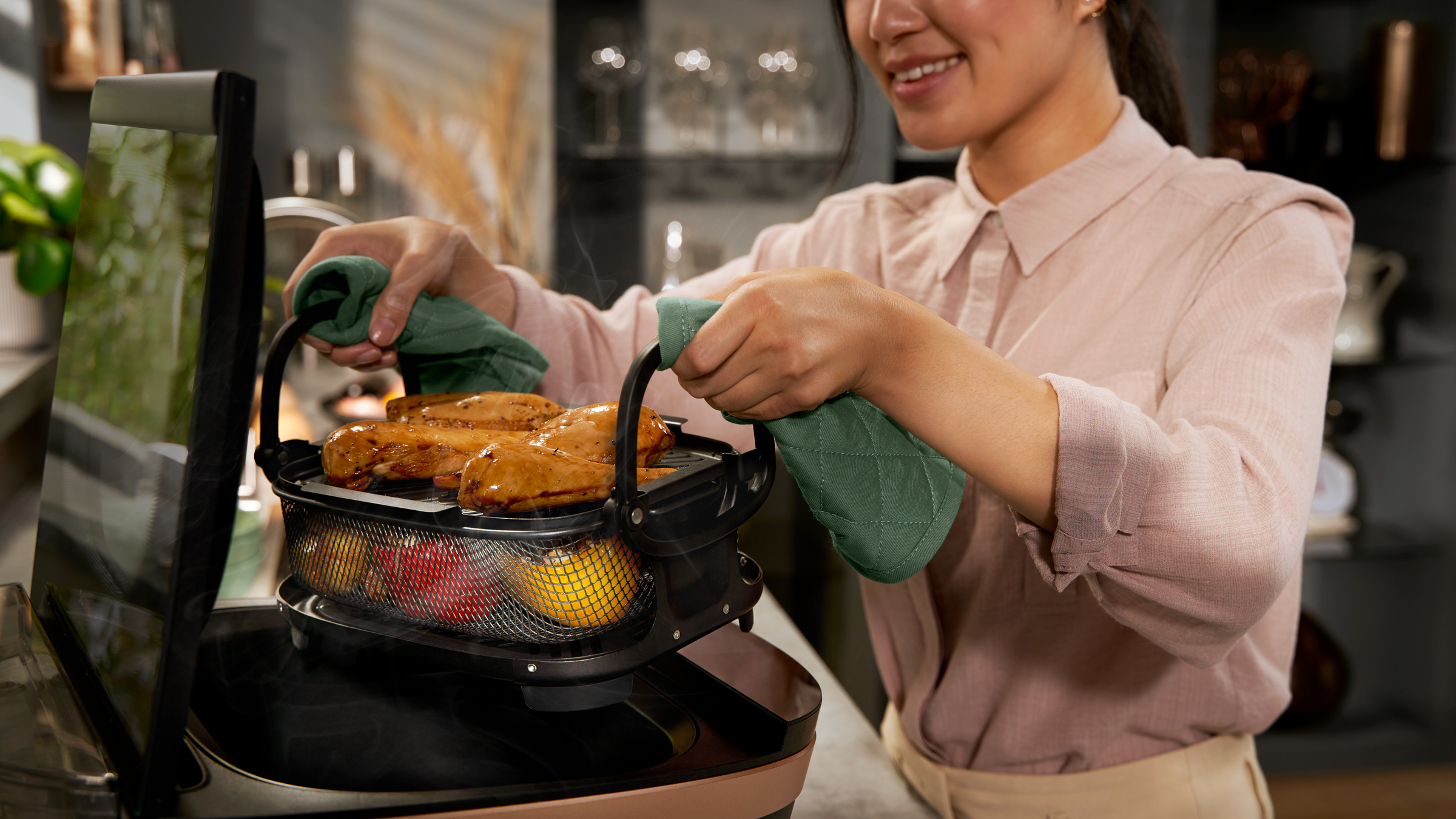 Vrouw die eten grilt in een aanrechtgrill, met ovenwanten, in een moderne keuken.