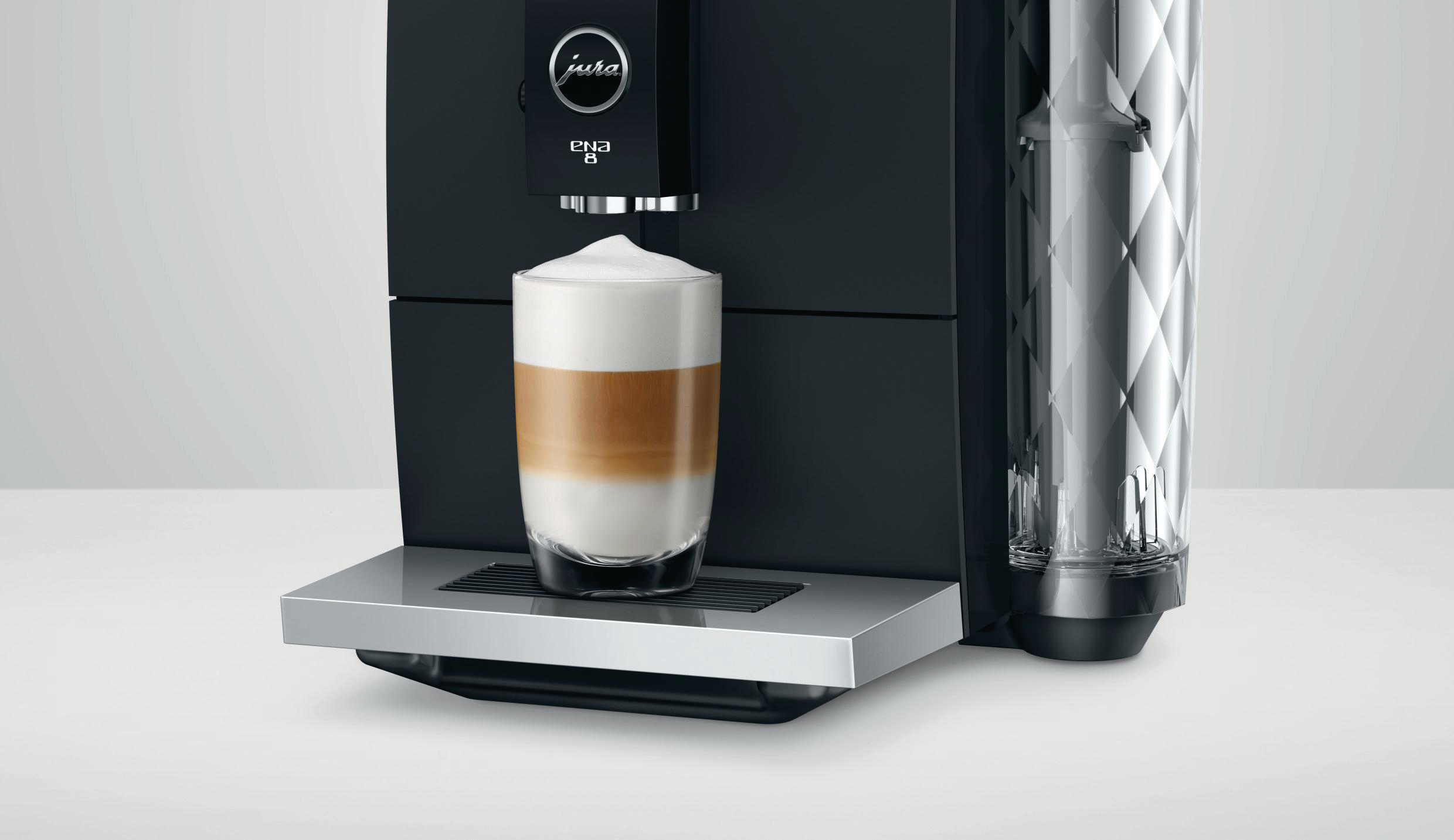 Eine Jura ENA 8 Kaffeemaschine. Ein Glas Latte Macchiato steht unter dem Kaffeeauslauf.