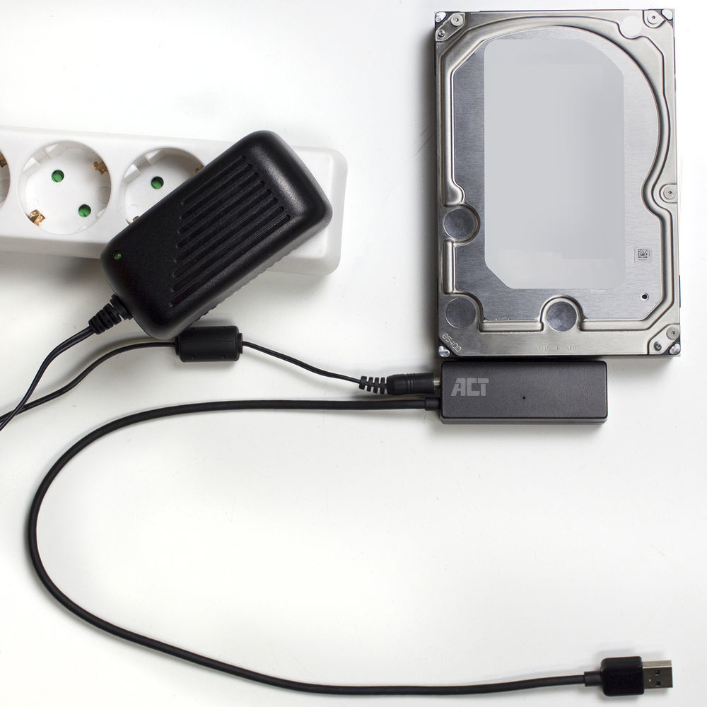 Hard drive connected to a power adapter and a USB cable on a white surface.
