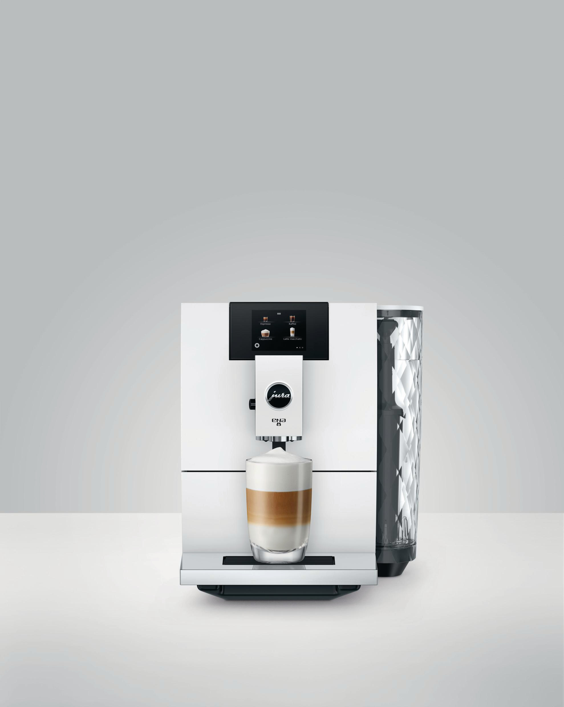 Weiße Jura Kaffeemaschine mit einem Glas Latte Macchiato vor hellgrauem Hintergrund.