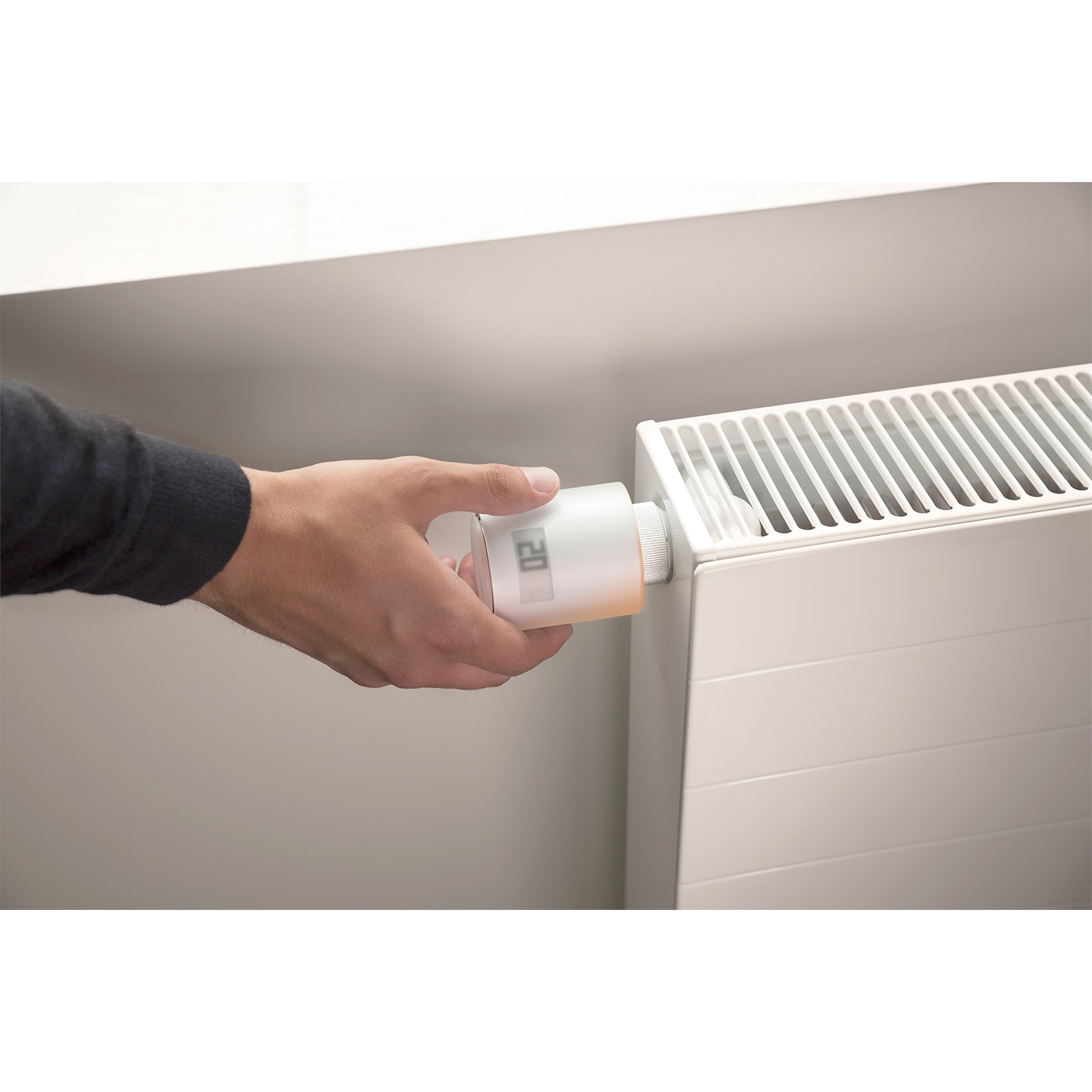 Una mano regola un termostato digitale bianco collegato a un radiatore bianco, mostrando il numero 20.