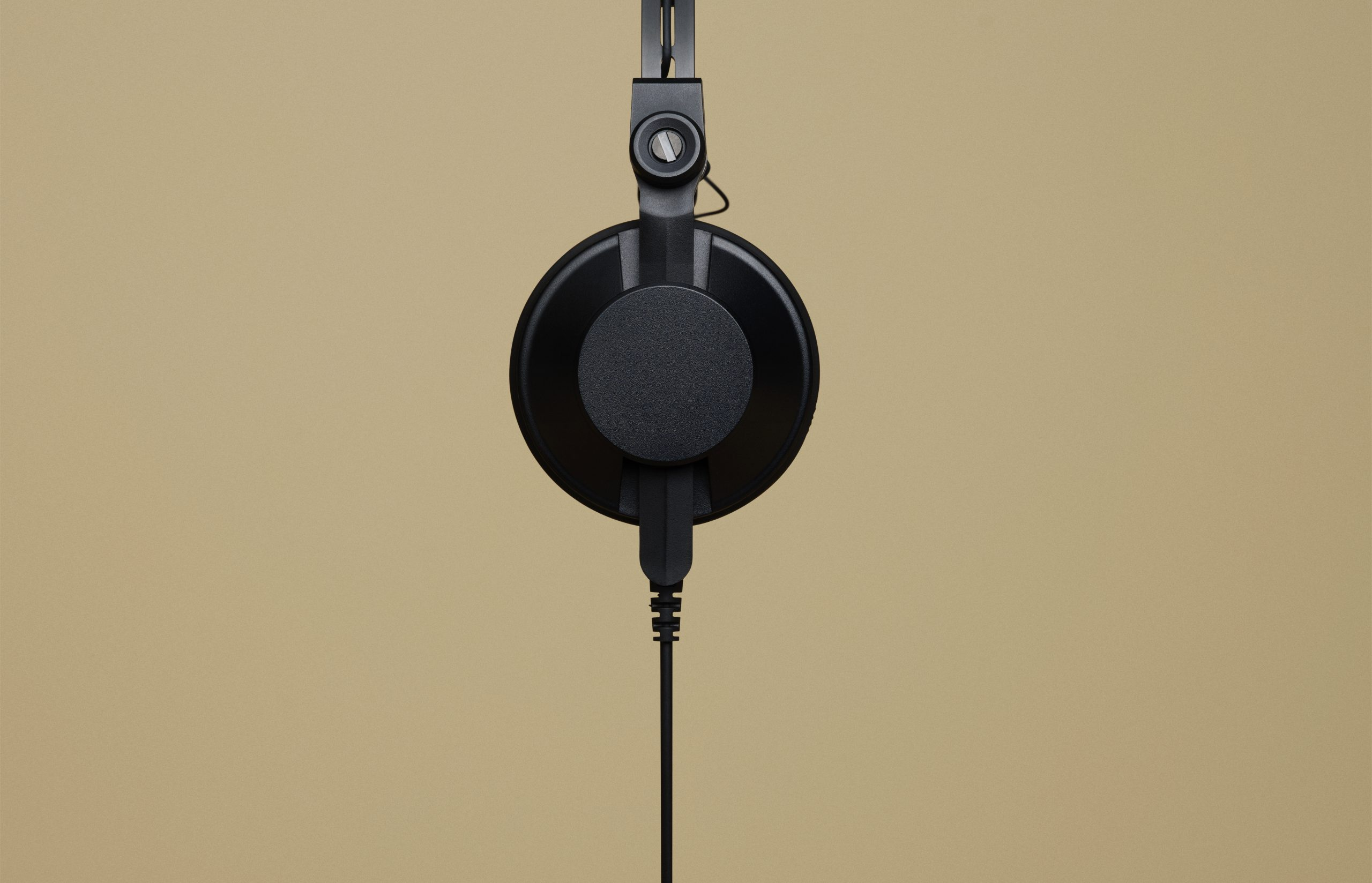 Black headphones with a cord, hanging against a beige background.