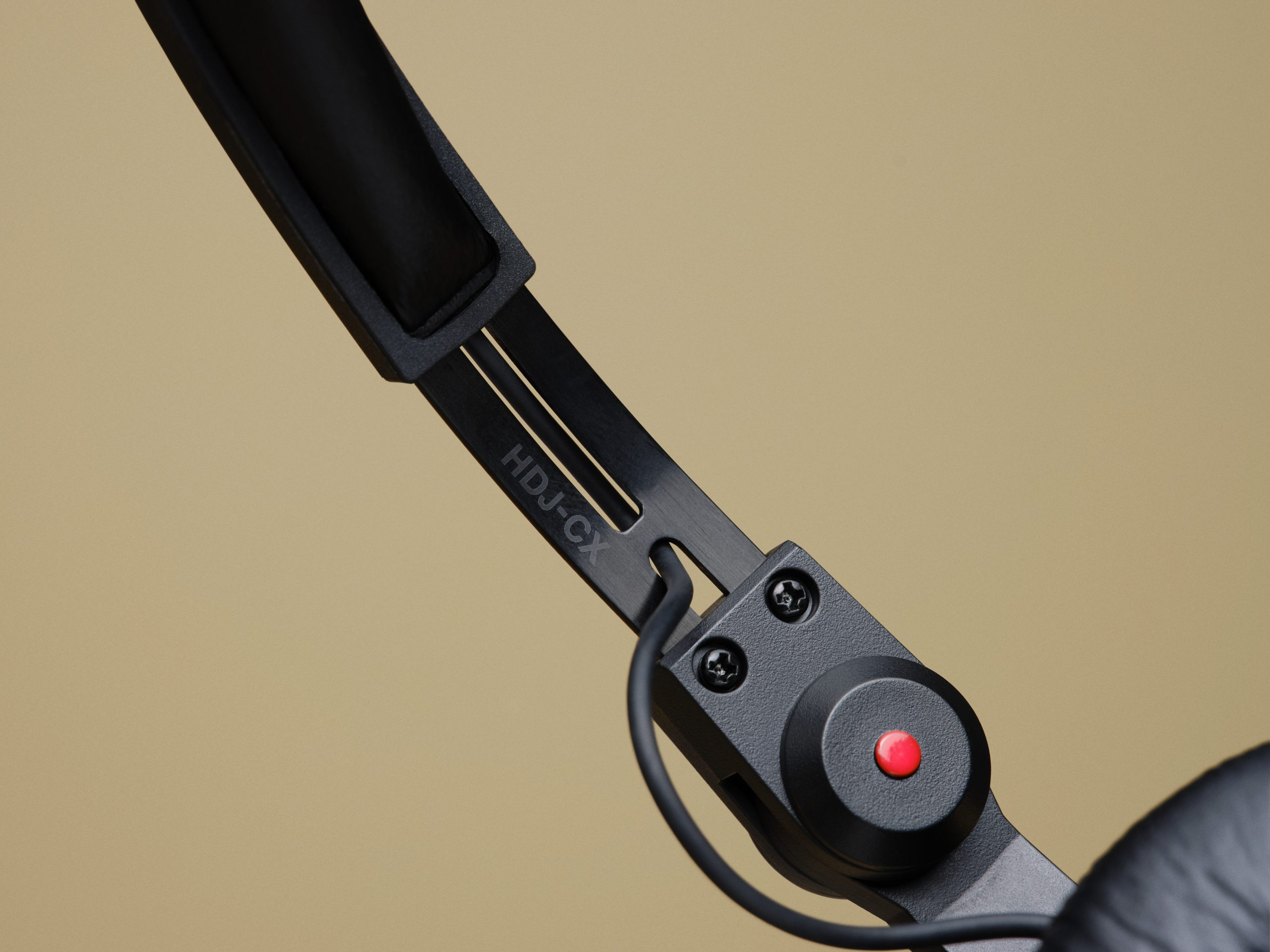 Close-up of black HDJ-CX headphones with a red button on a beige backdrop.