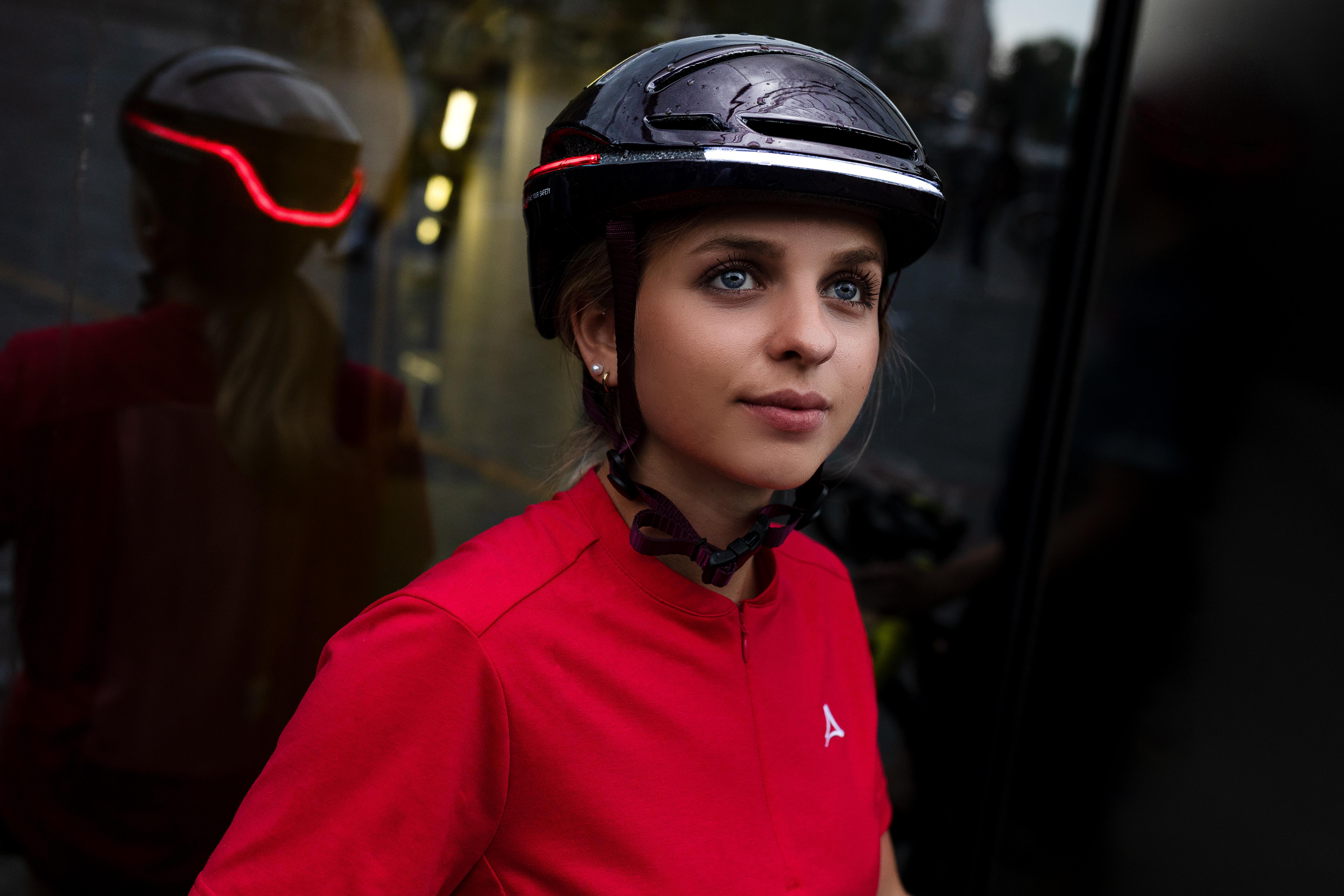 Frau mit Helm. Rotes Hemd, schwarzer Helm mit rotem Licht. Gebäude und Stadt verschwommen.