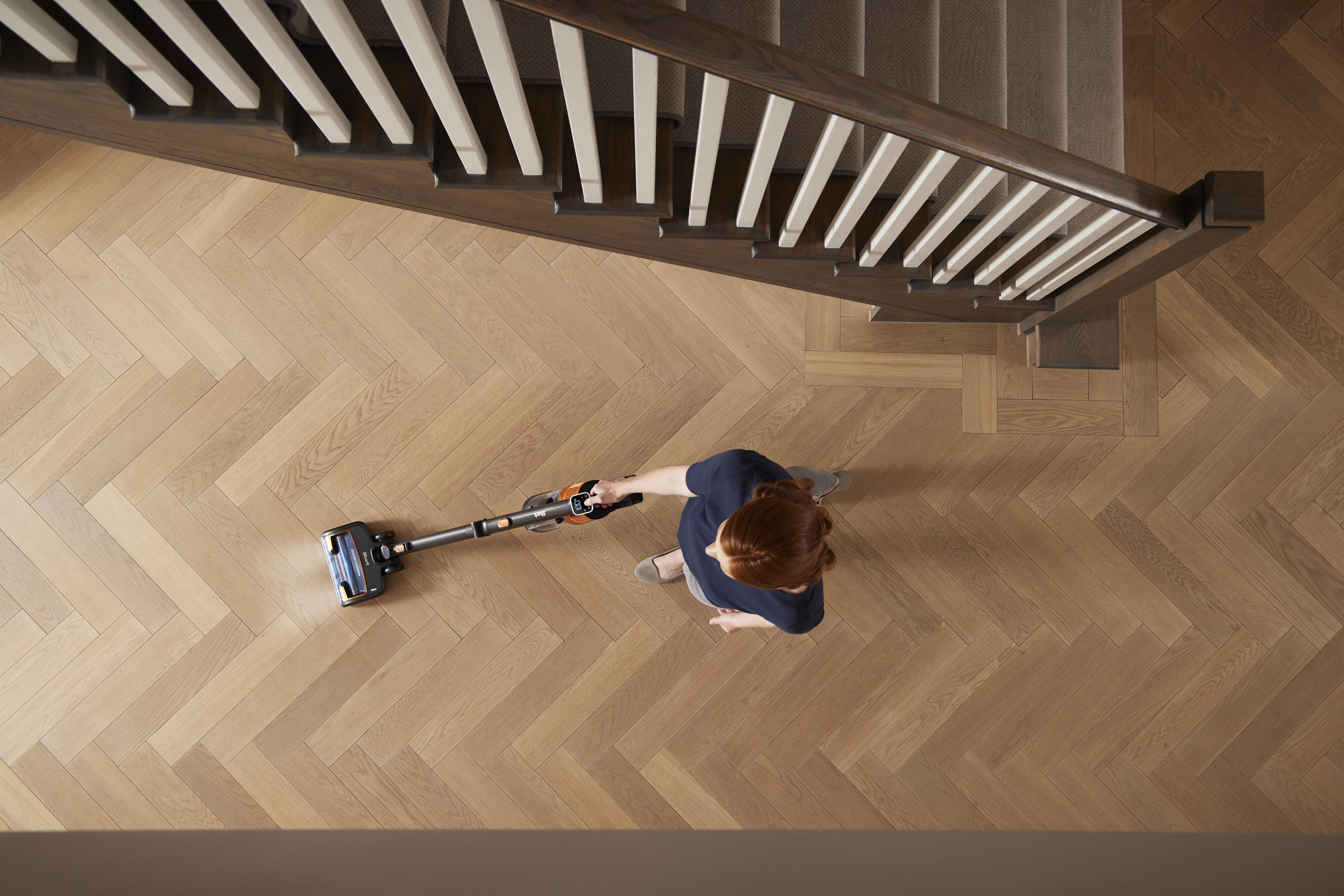 Frau saugt Holzboden mit Treppe im Hintergrund. Draufsicht.