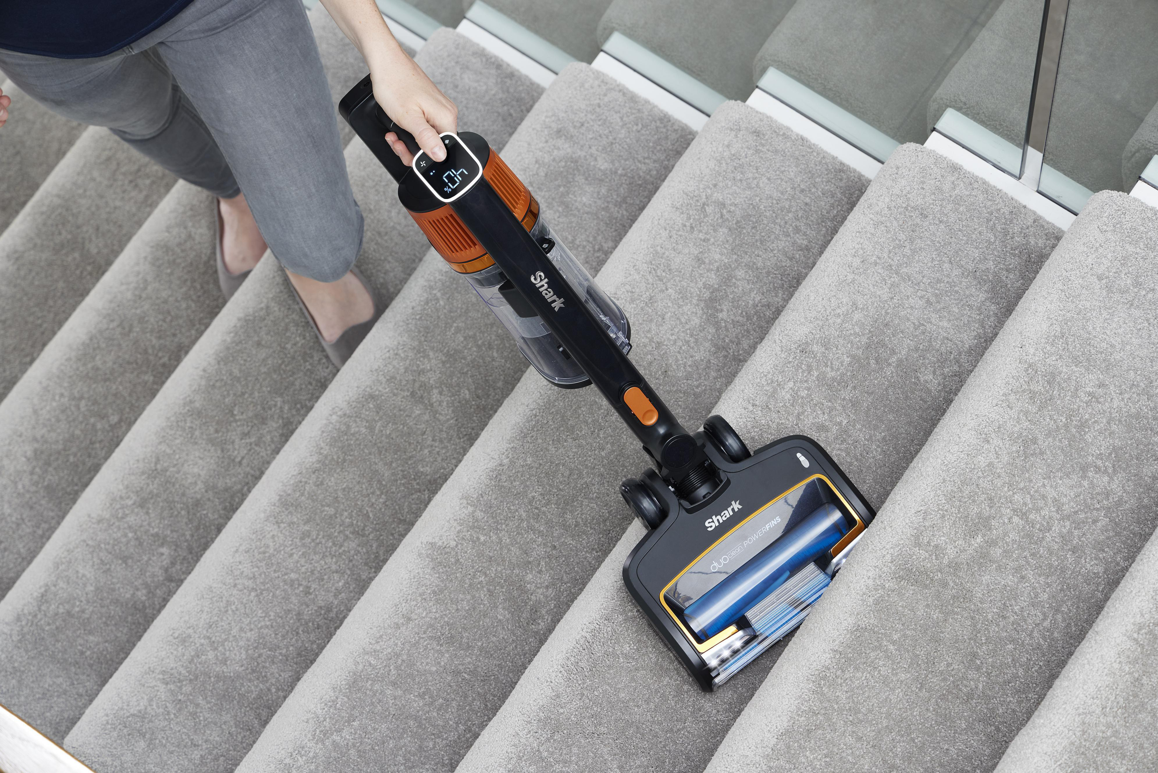 Eine Frau benutzt einen schwarz-orangenen Staubsauger auf grauem Teppich auf einer Treppe.