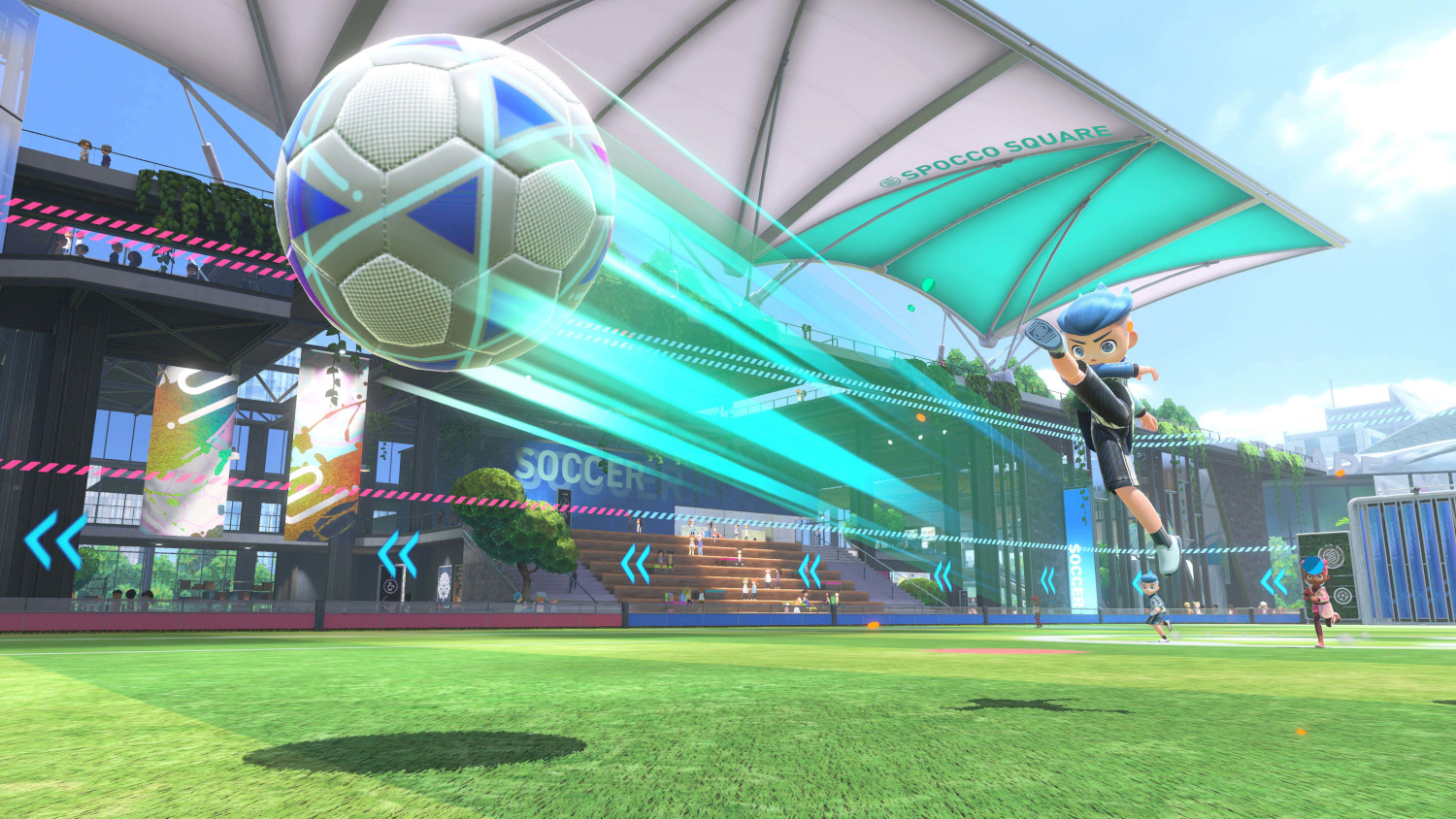 A soccer player kicks a soccer ball in a stadium. Other players and a crowd are present.