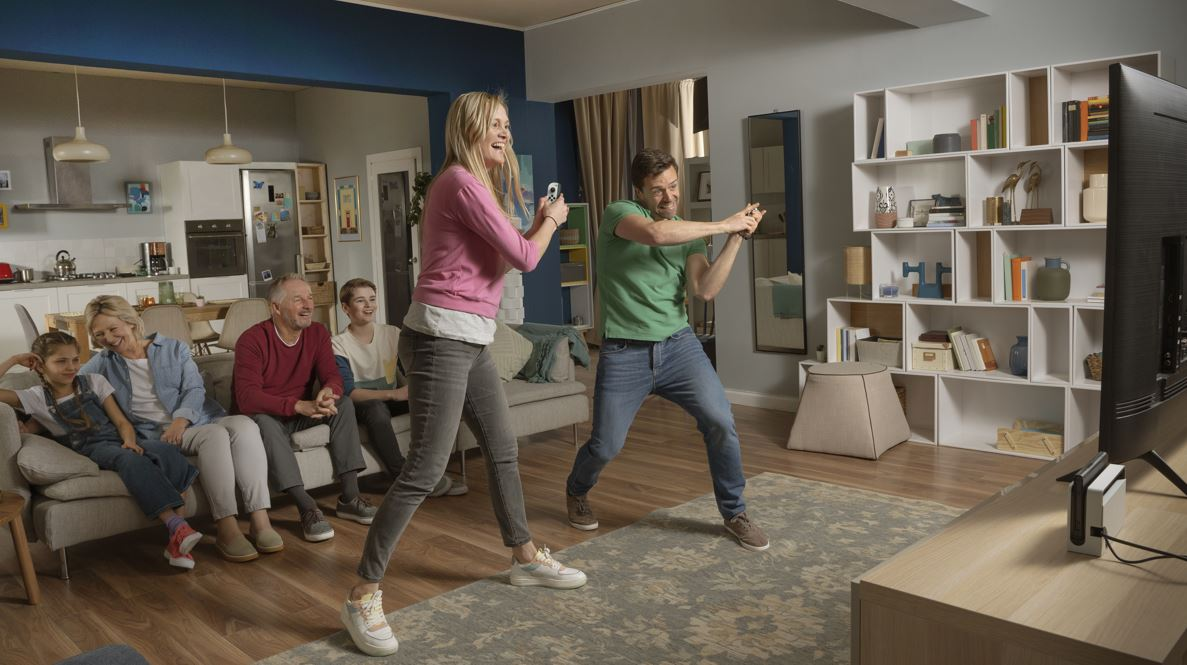 Family playing video game with controllers, in a living room setting.