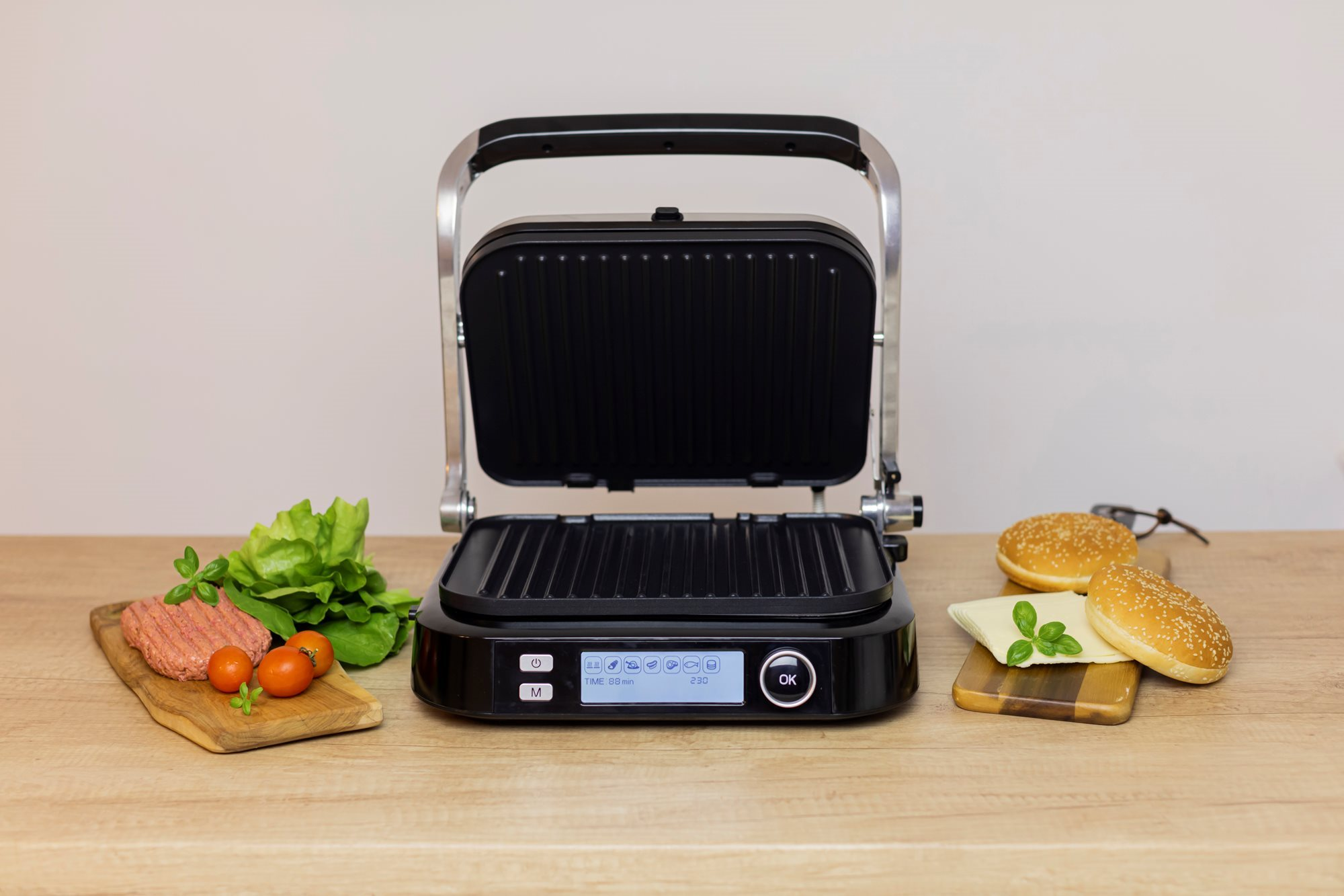 Nyitott fekete grill élelmiszerekkel egy fa deszkán. Burgerek, paradicsom, saláta, kenyér.