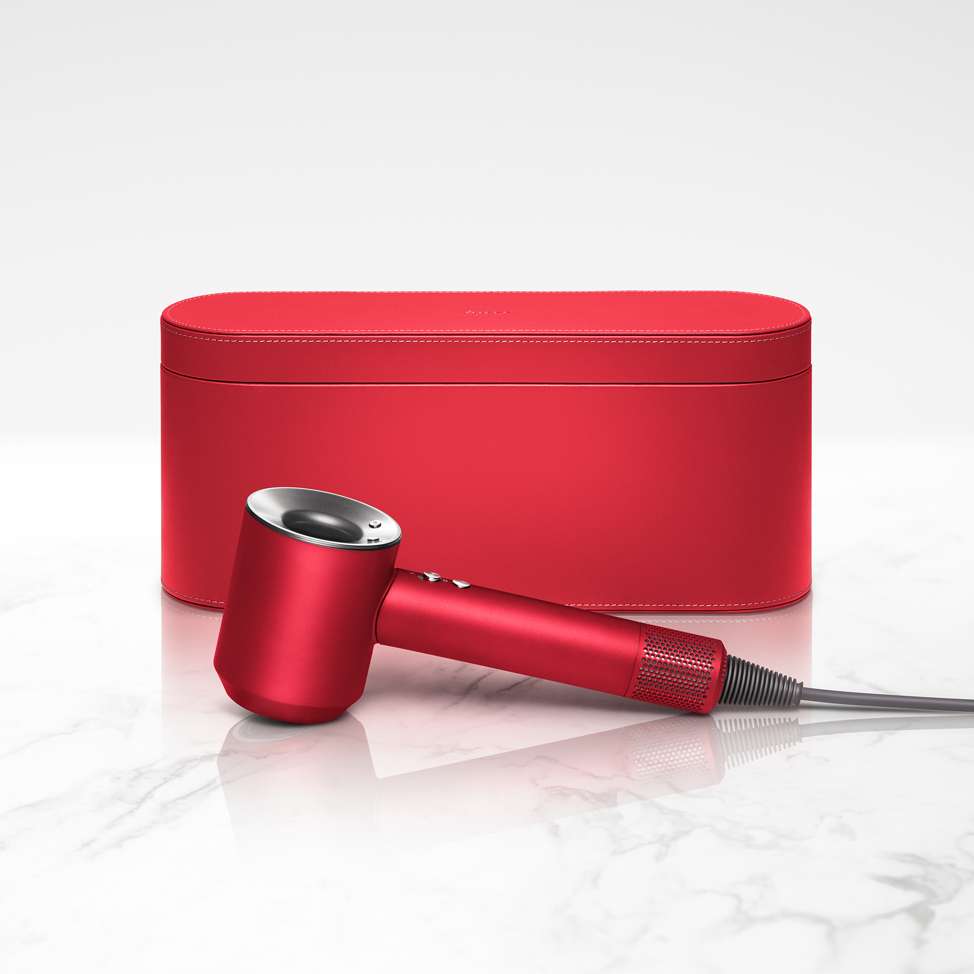 Ein roter Dyson Haartrockner und Aufbewahrungskoffer auf Marmoroberfläche.