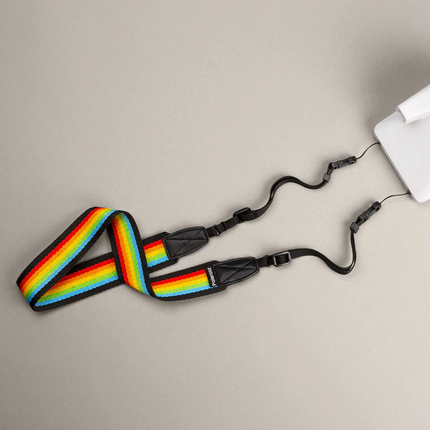 Una correa de cámara colorida con un patrón de arcoíris. La correa está sujeta a una cámara blanca.
