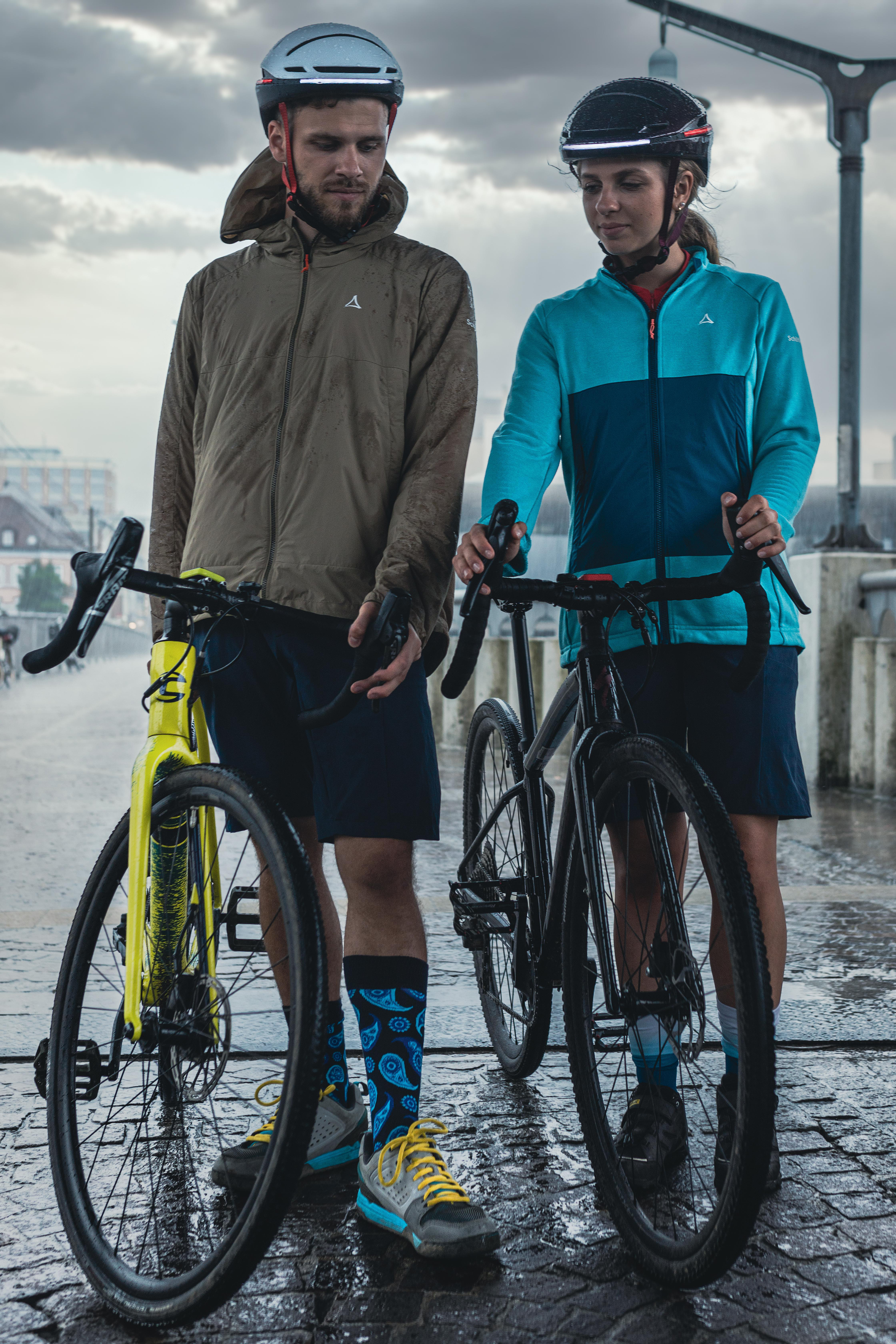 Zwei Radfahrer mit Fahrrädern, eins gelb und eins schwarz, stehen auf nassem Untergrund.