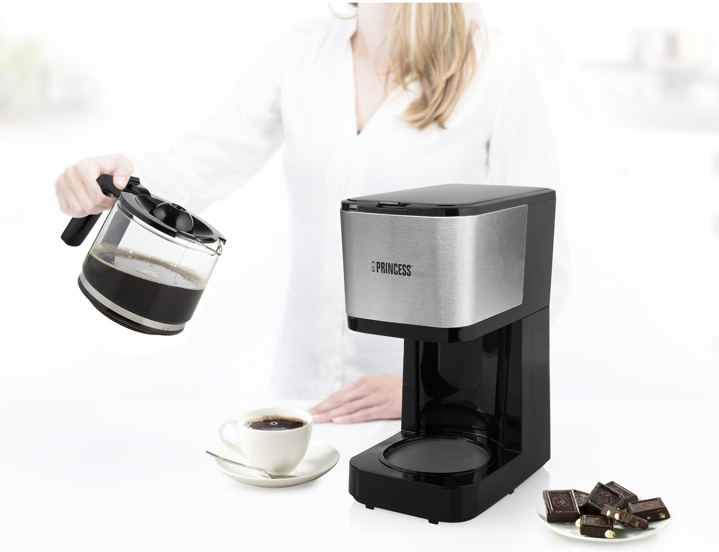 Donna che versa caffè da una caraffa di vetro in una tazza. Macchina del caffè sullo sfondo.