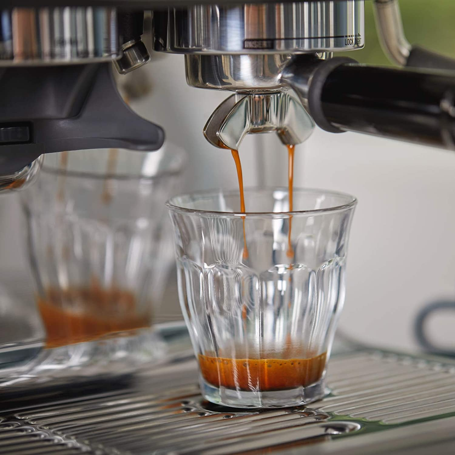 Máquina de espresso dispensando café en una taza de vidrio, vista de cerca.