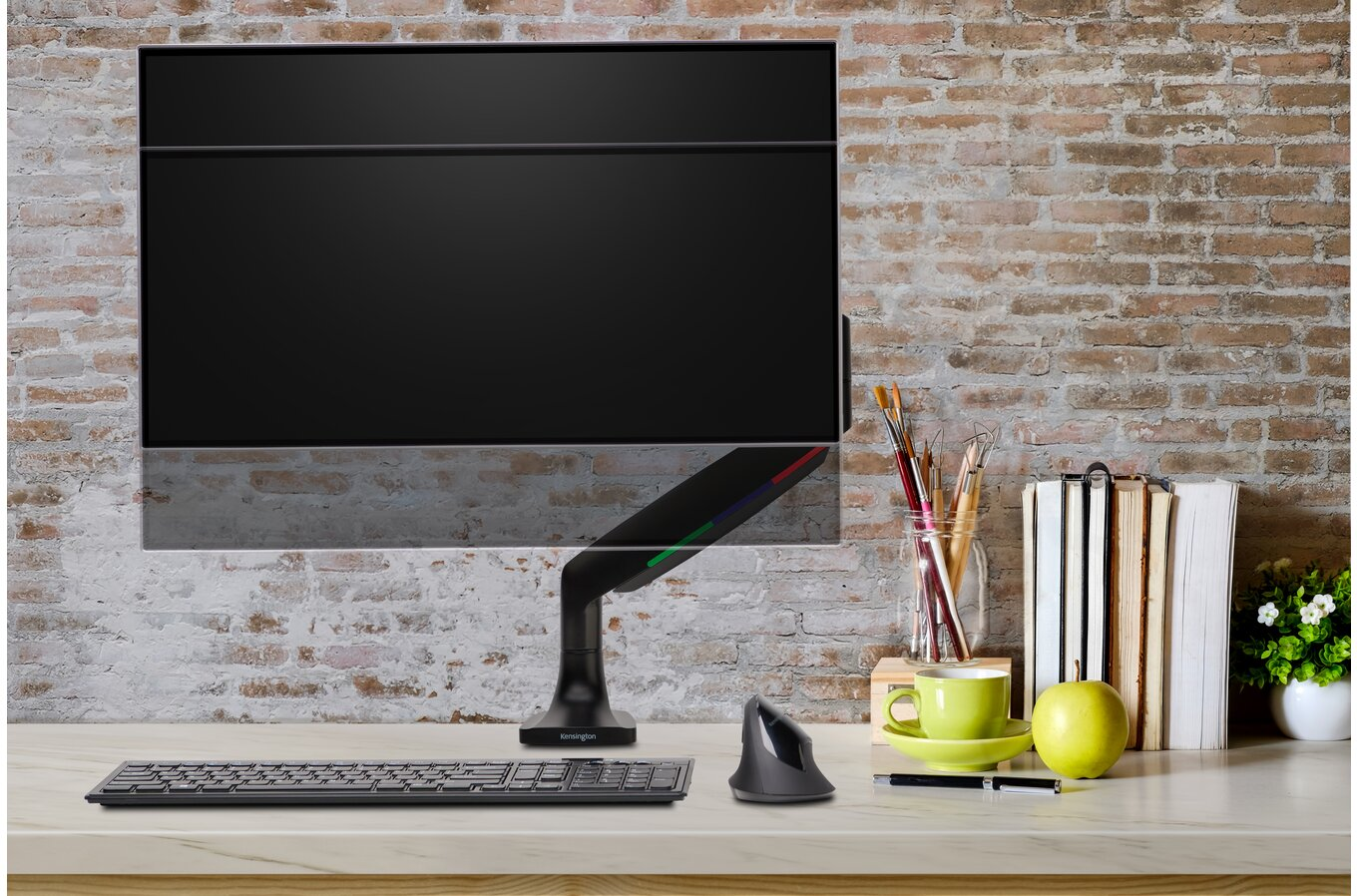 Egy karra szerelt számítógép monitor, billentyűzettel, egérrel és íróasztali tárgyakkal egy téglafal hátterében.