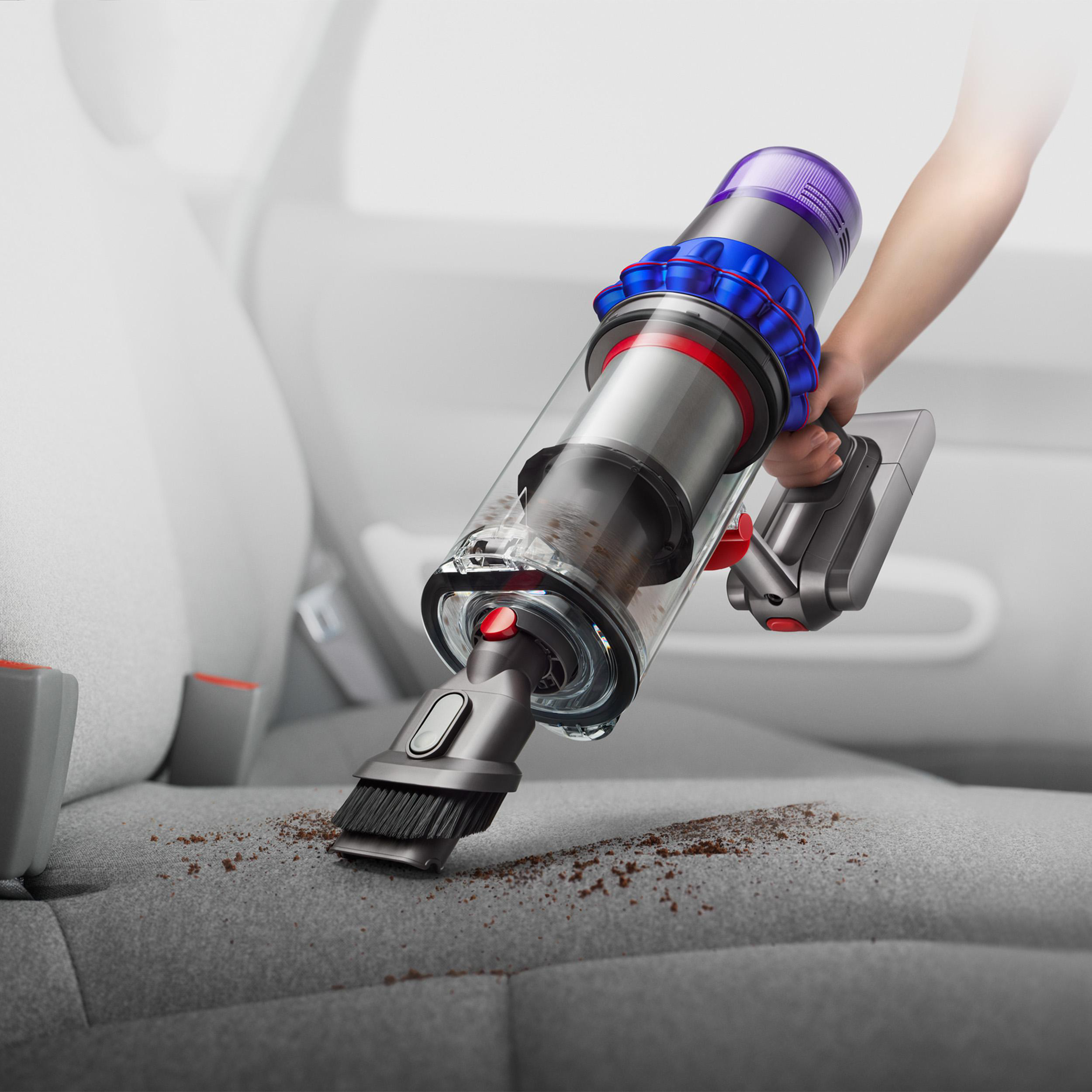 Eine Hand hält einen Staubsauger über einem Autositz und reinigt Schmutz. Der Staubsauger ist silbern und blau.