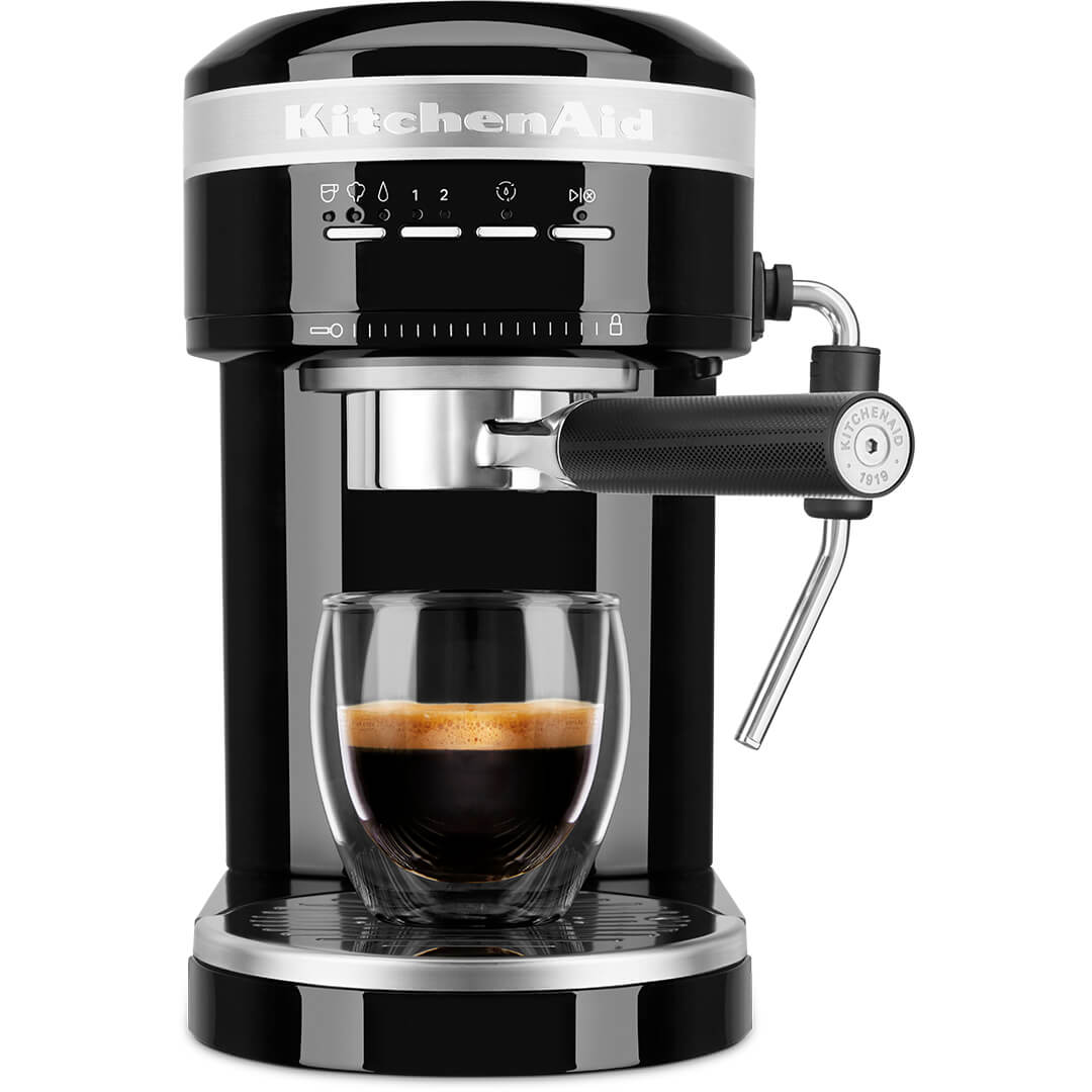 Egy fekete KitchenAid eszpresszó gép egy pohár kávéval. Fehér háttéren van.