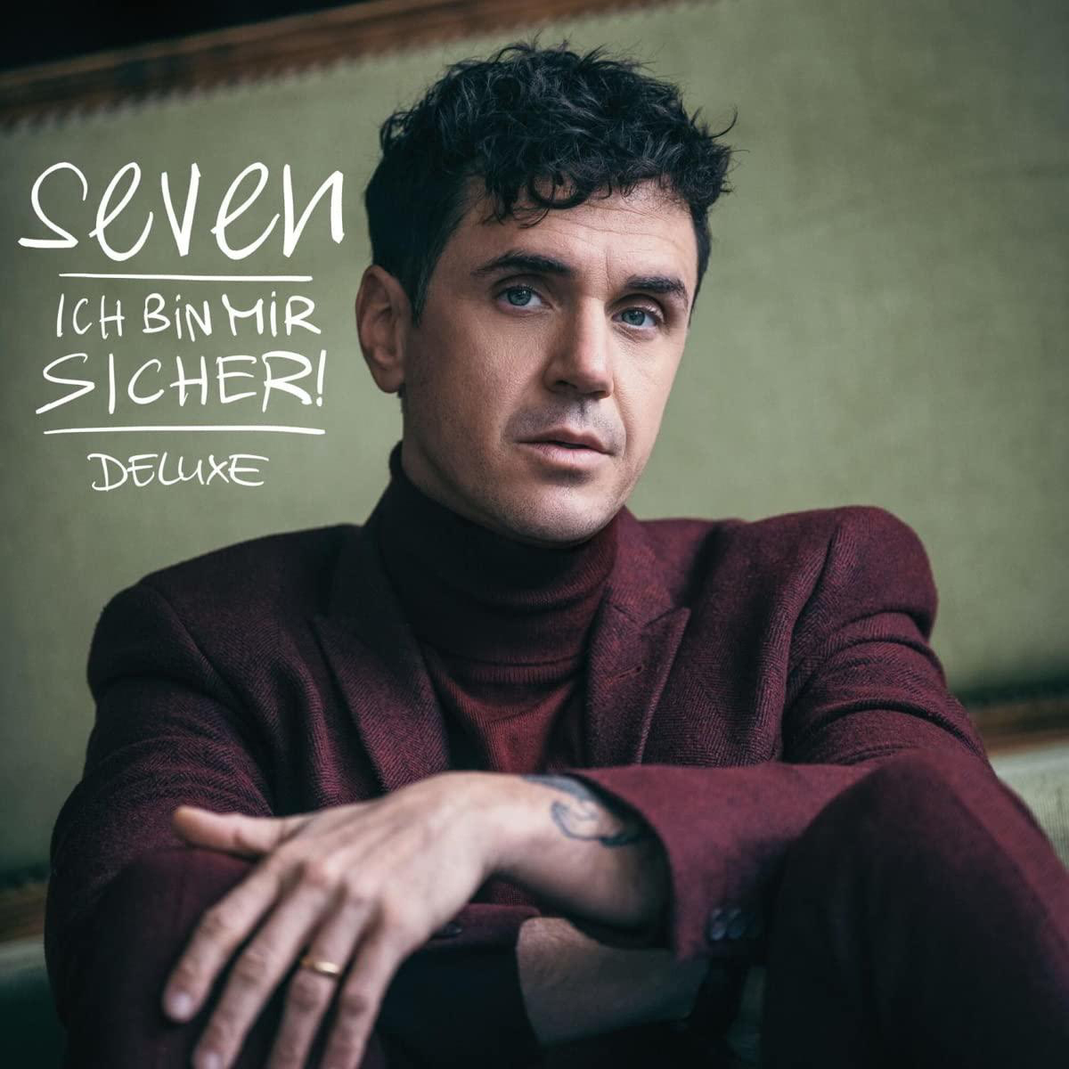 Mann in bordeauxfarbenem Anzug. Albumcover mit dem Titel "Seven" und Künstlername.