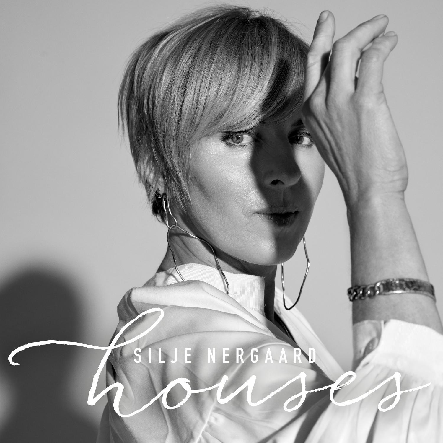 Schwarzweißfoto von Silje Nergaard mit kurzen blonden Haaren, Ohrringen und weißem Oberteil, Hand erhoben.