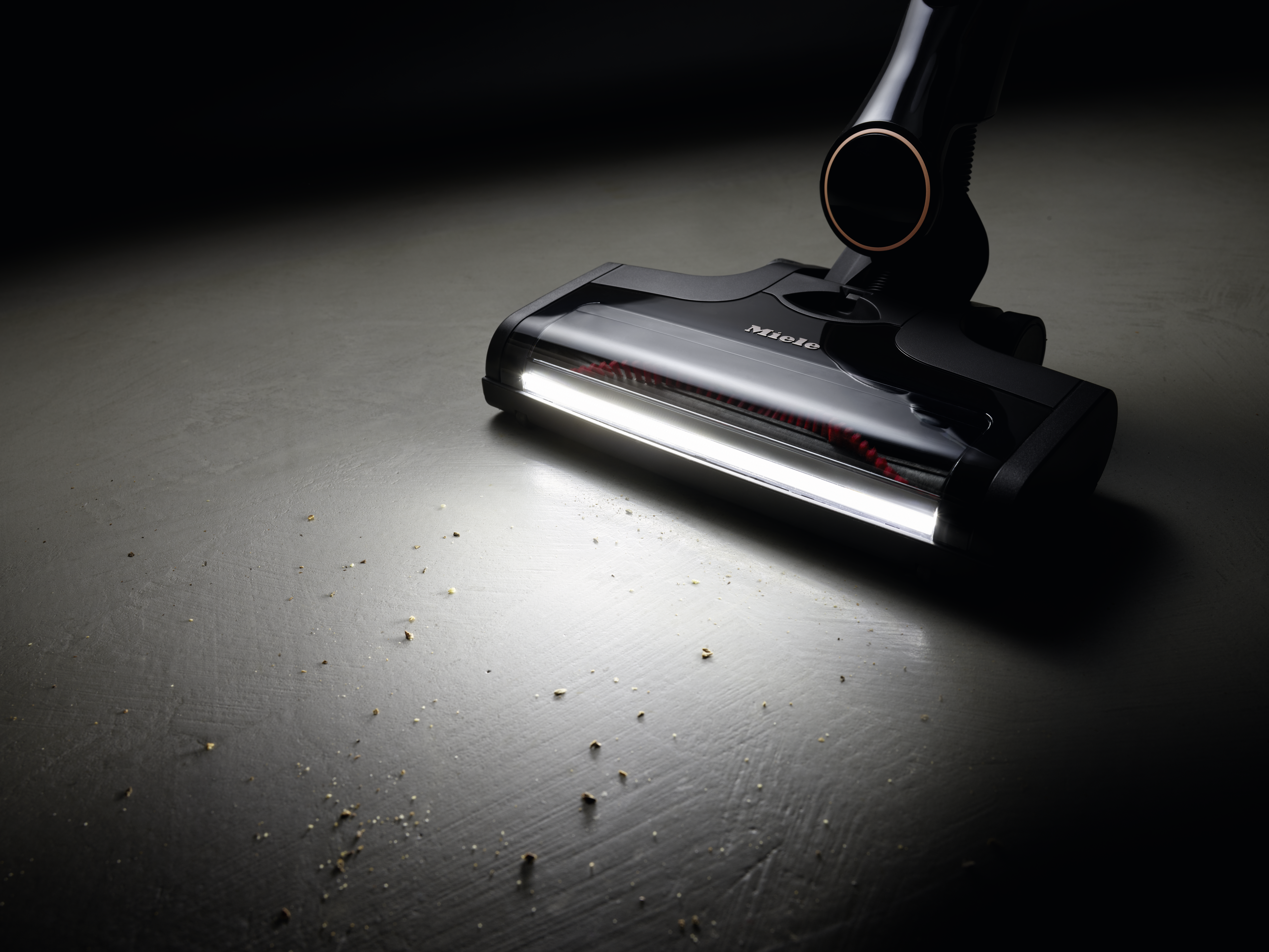Close-up of a vacuum cleaner head. A white light shines from the front, illuminating the floor.