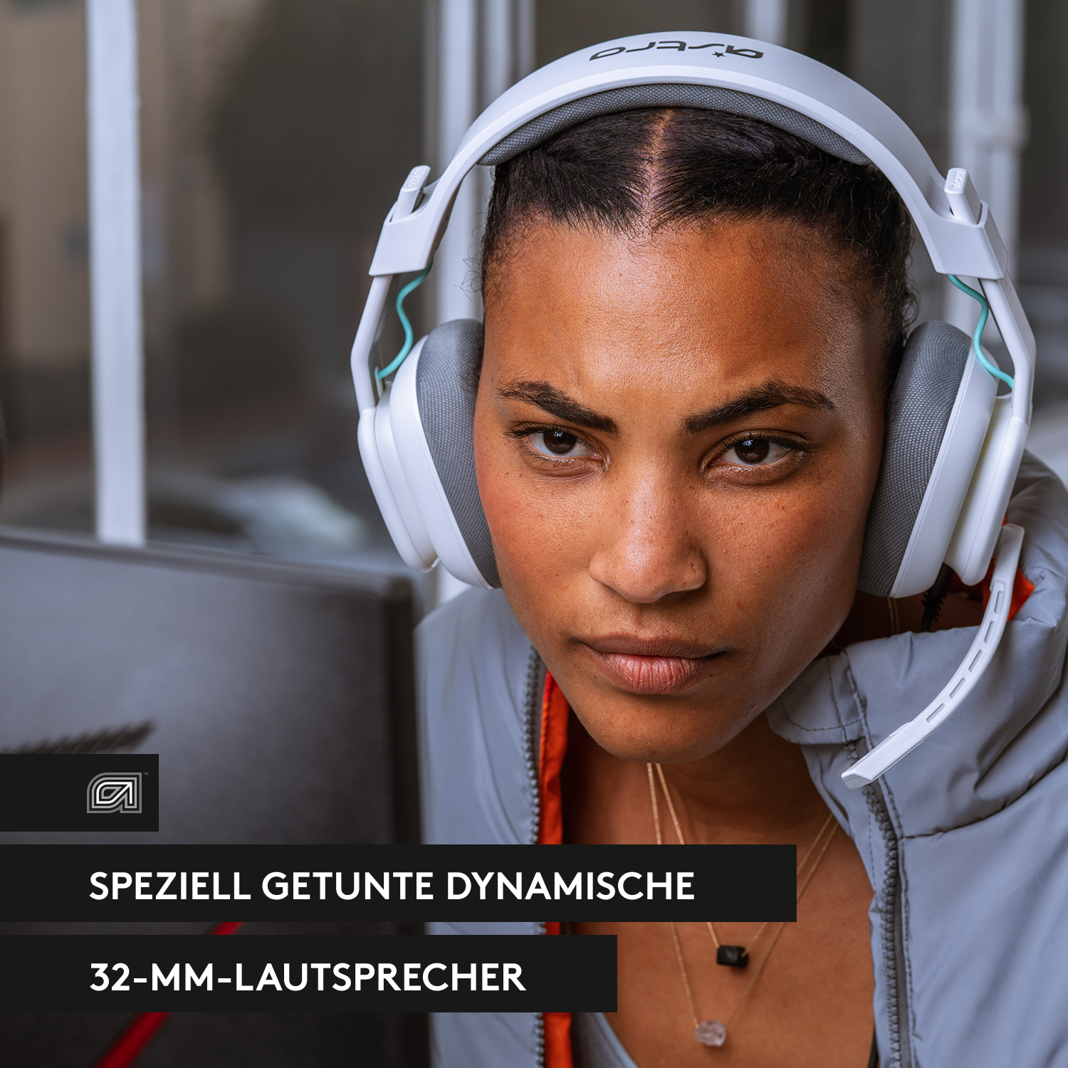 Eine Frau mit weißen Kopfhörern, die aufmerksam schaut. Ein Bildschirm ist im Hintergrund. Text auf dem Bild.