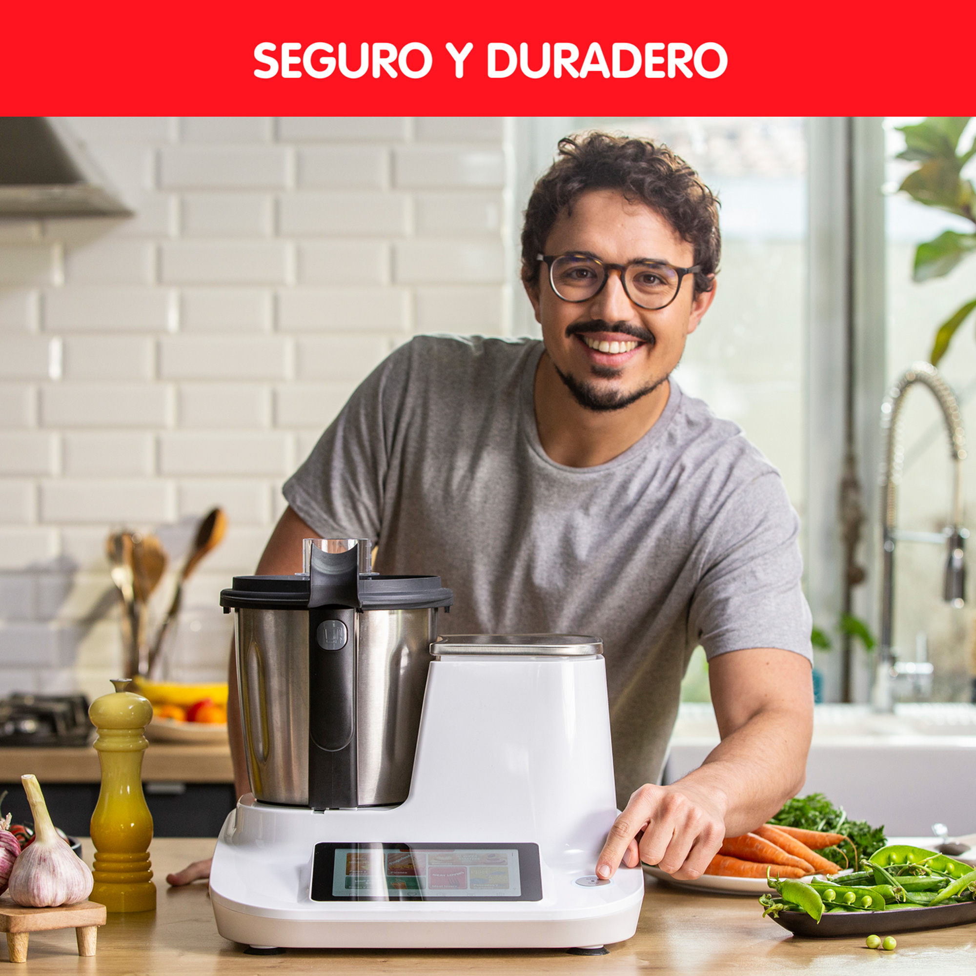 Un hombre sonríe mientras pulsa un botón en un electrodoméstico de cocina blanco. Hay verduras en la encimera.